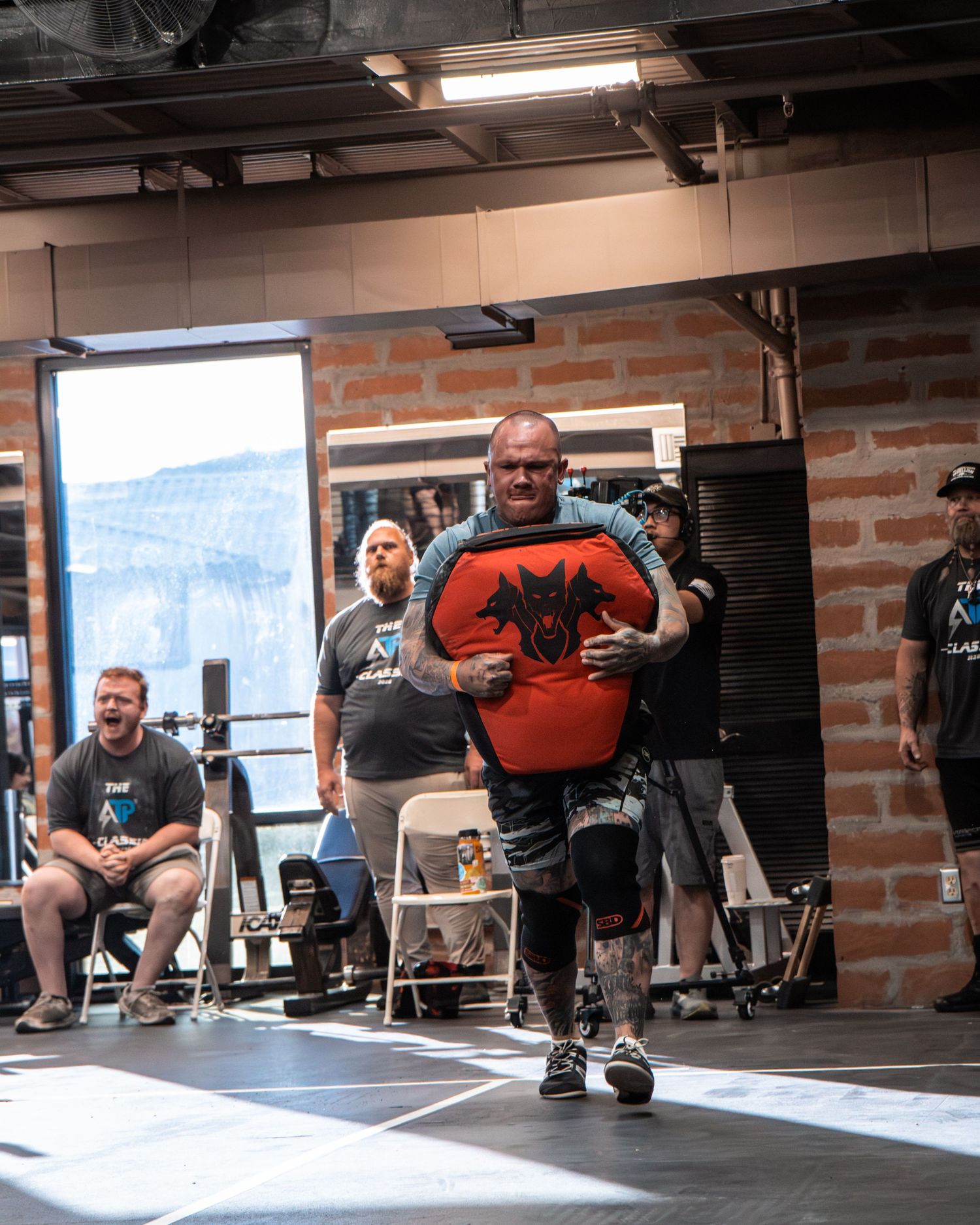 Athletes executing squats with barbells in a brick-walled training facility.
