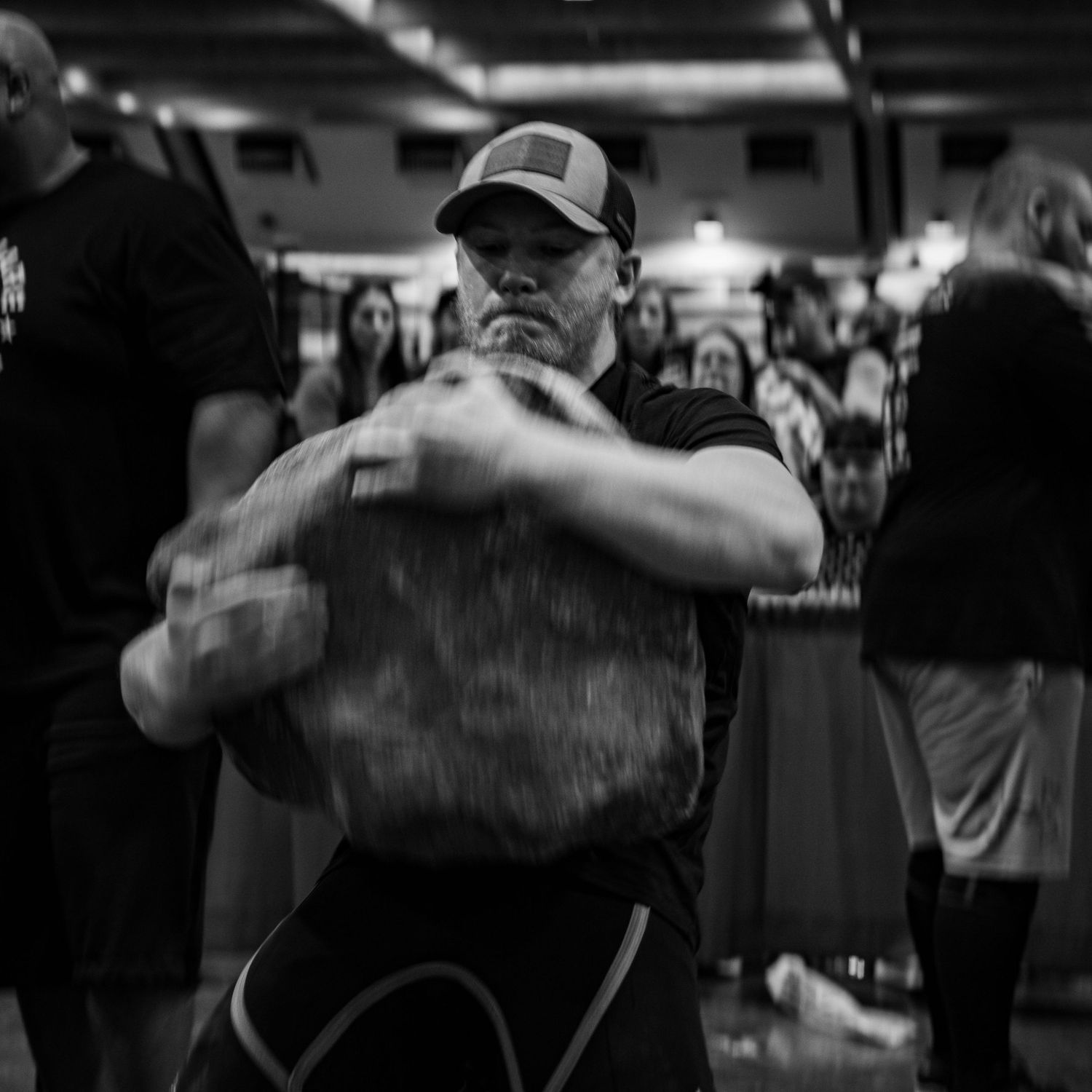 Athletes in a gym perform intense workouts with barbells and weights in black and white.