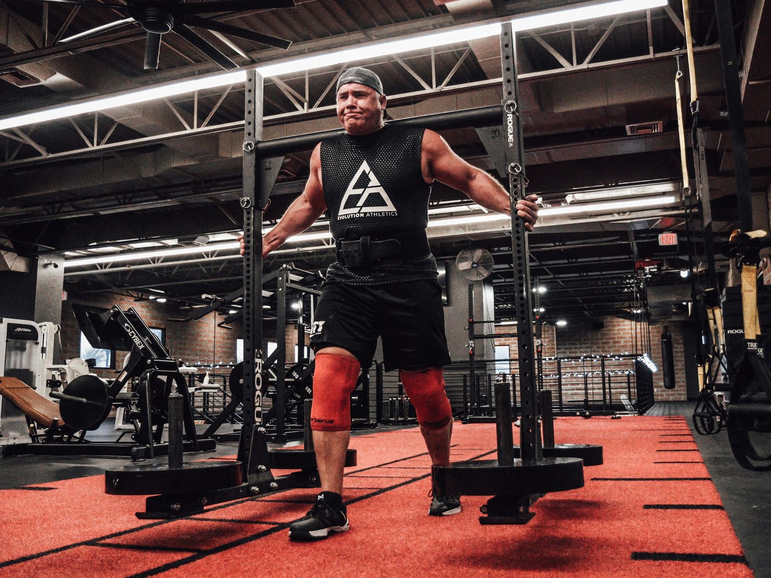 Red-floored gym interior with weight equipment and training stations.
