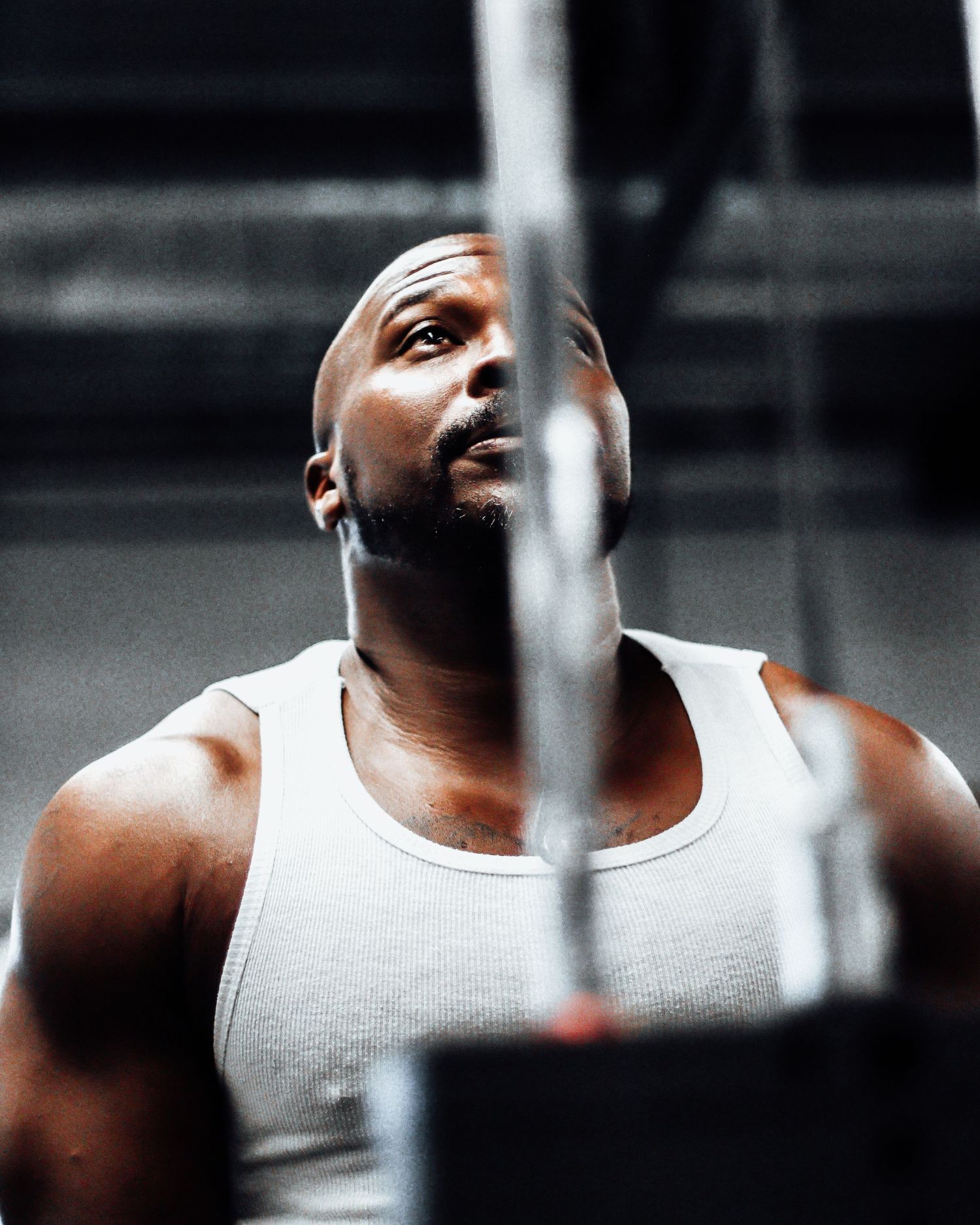 Person in white tank top exercising at gym equipment with dramatic lighting.