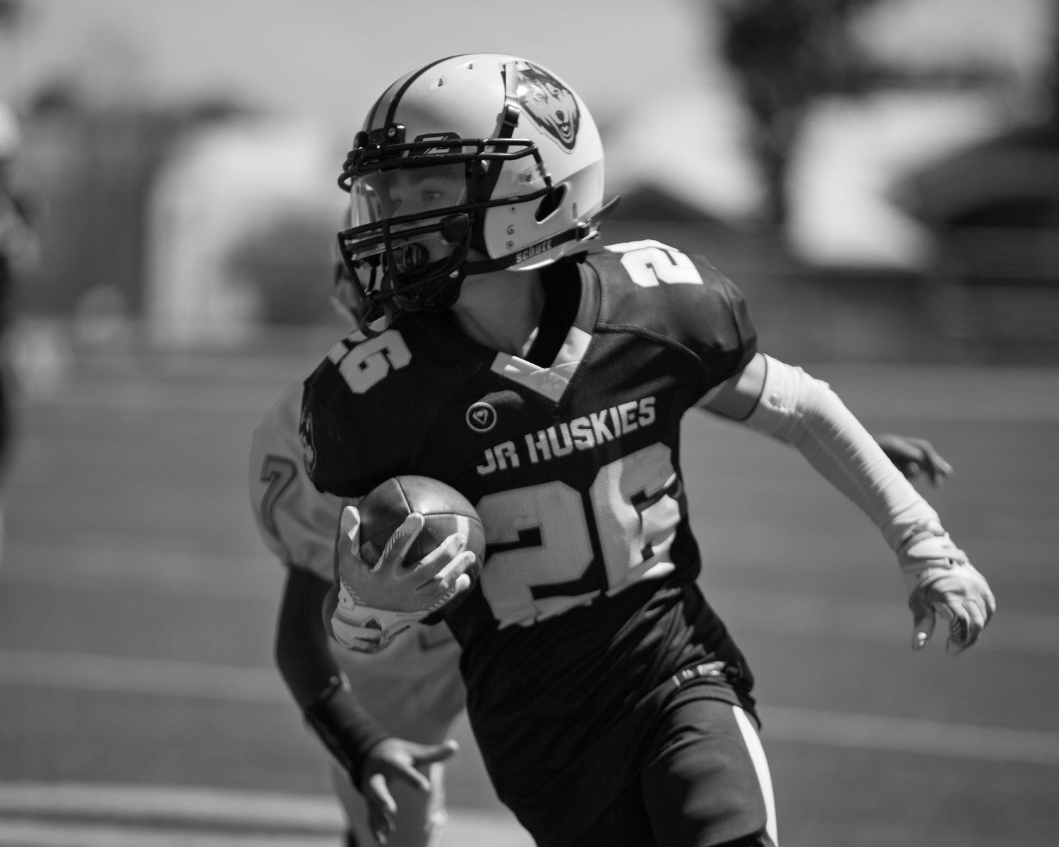 Young football player in JR Huskies jersey number 26 running with the ball during a youth league game.