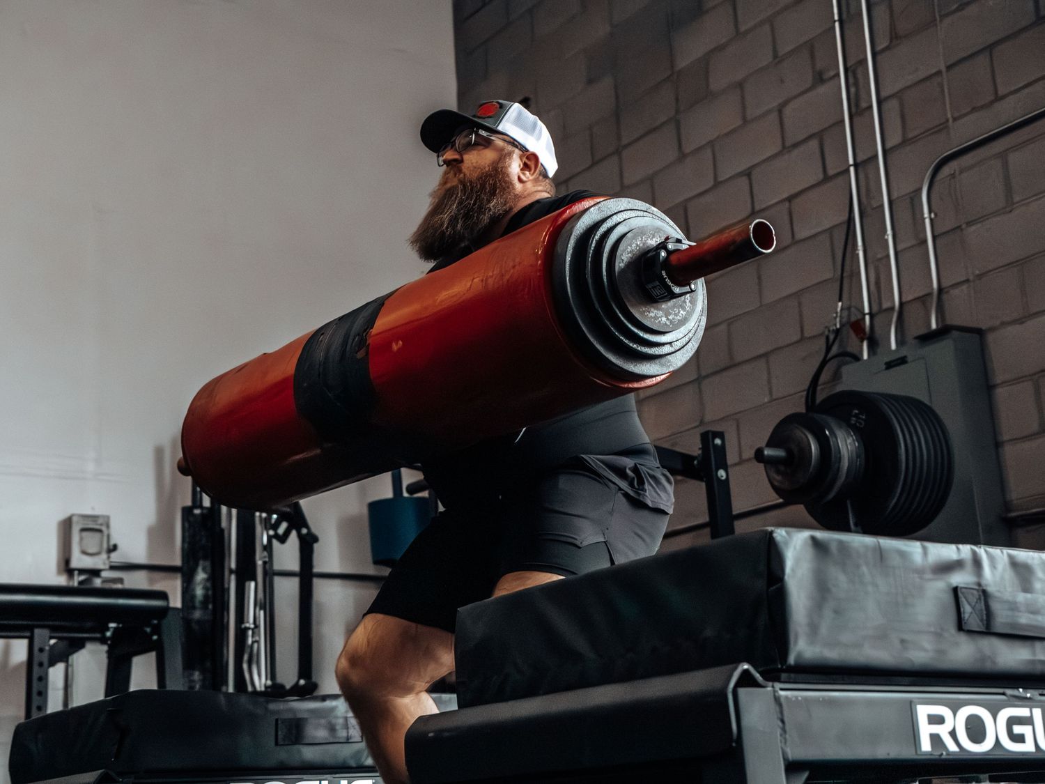 Close-up of weightlifting equipment and barbell setup against brick wall in gym setting.