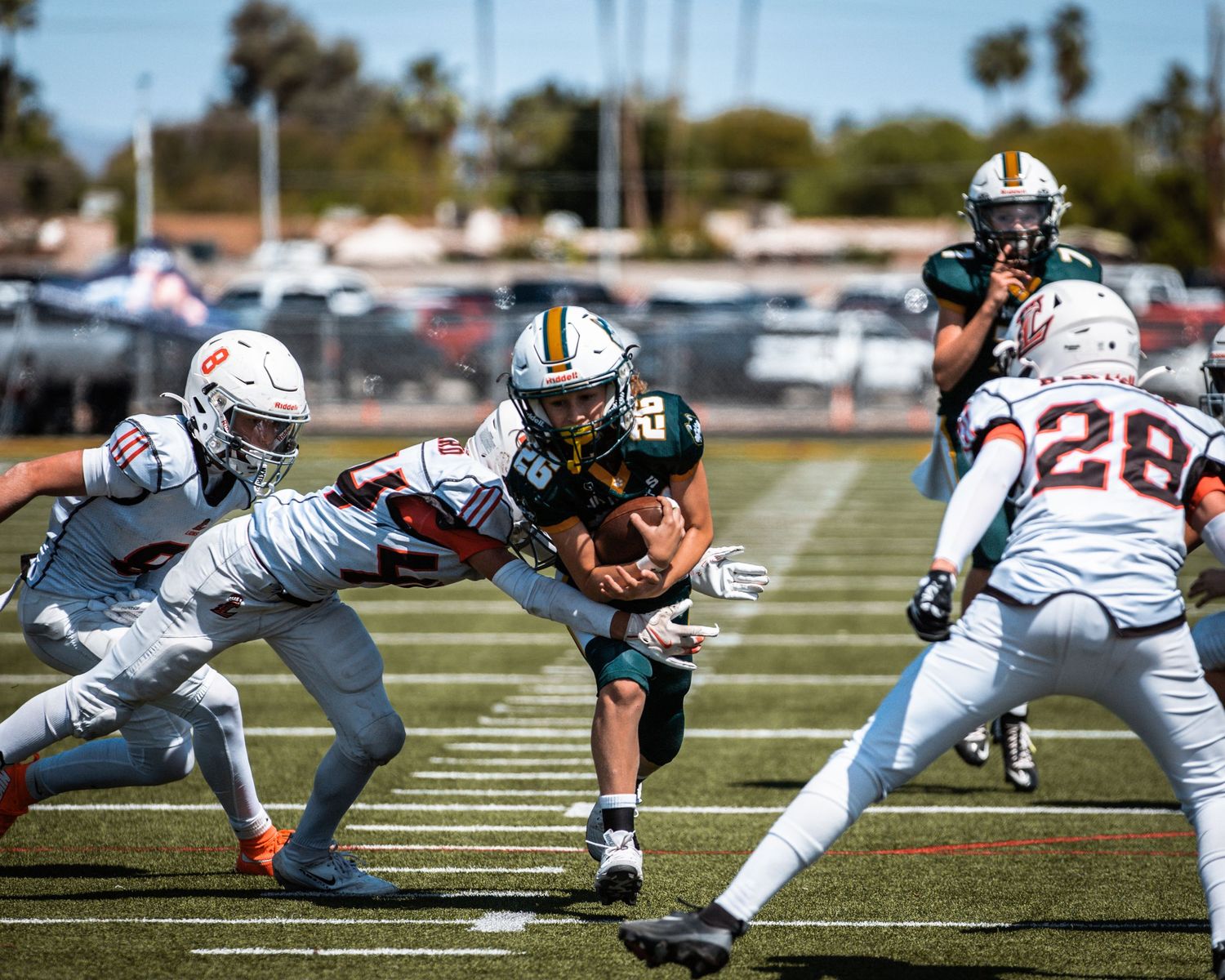 Football player in gold uniform breaks through defenders during a sunny outdoor game on a green turf field.