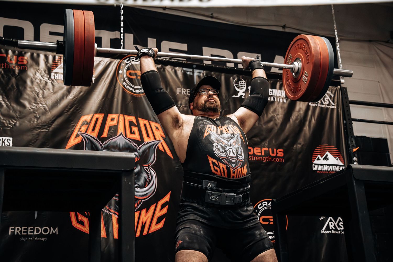Athlete performing successful overhead barbell lift against dark gym backdrop.
