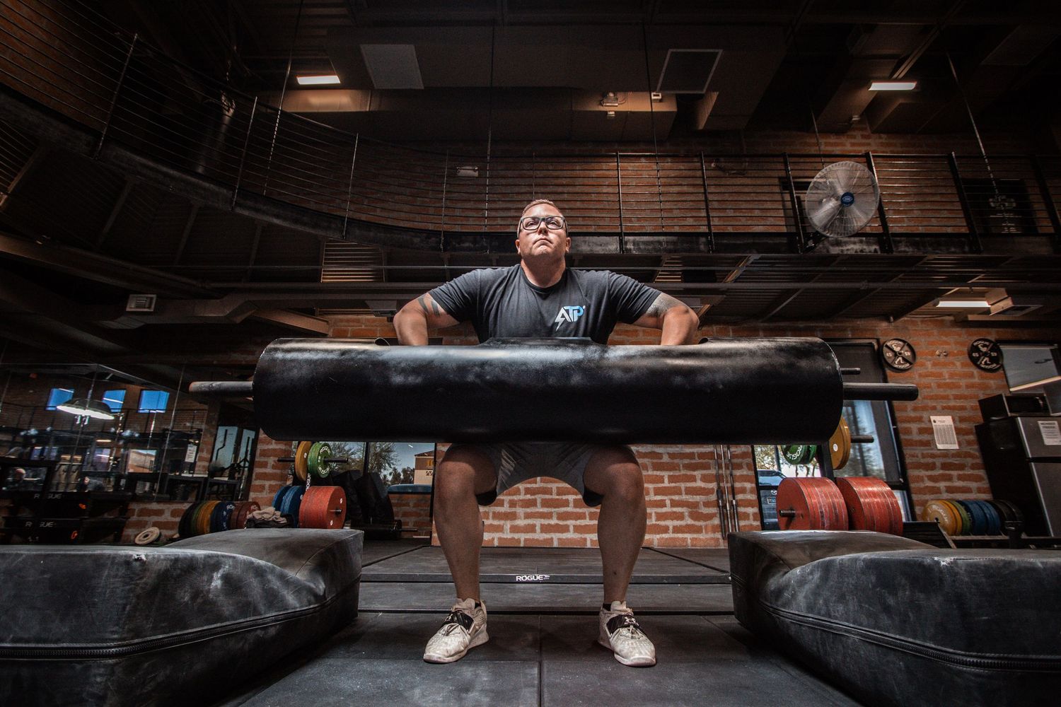 Man performing a heavy deadlift with large bumper plates in a dark industrial gym setting.