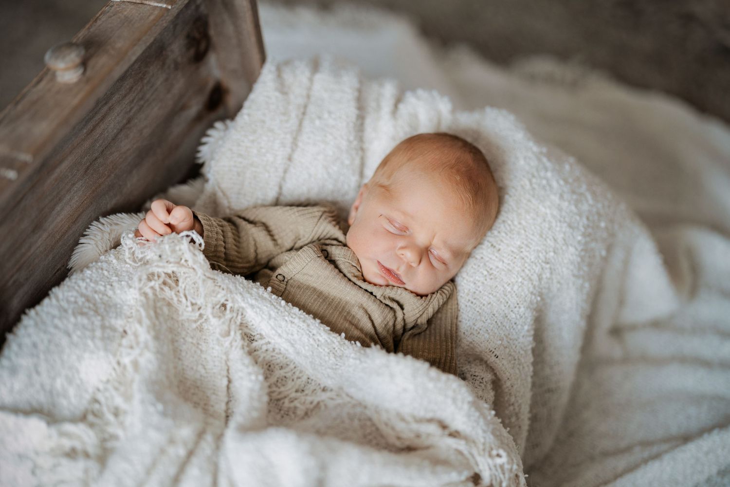 Peaceful newborn baby sleeping wrapped in soft cream blanket inside rustic wooden crate, newborn photography.
