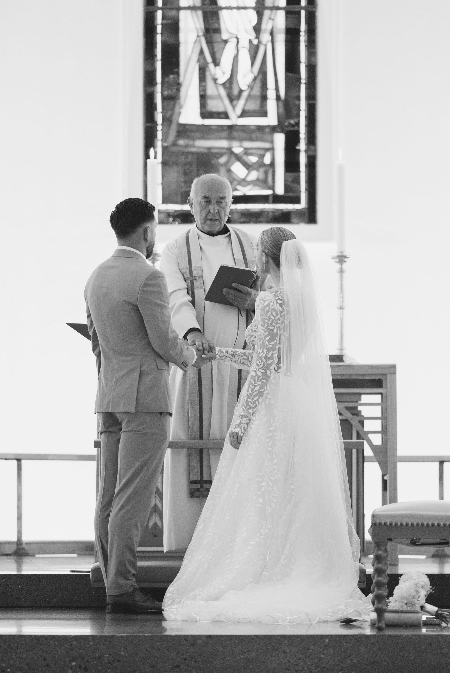 A black and white photograph of a wedding ceremony in a church with a couple and officiant standing at the altar.