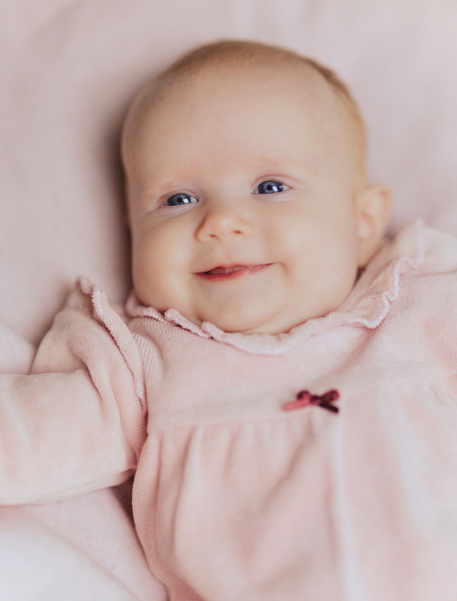 A series of sweet baby portraits in soft pink clothing showing different expressions against a light background.