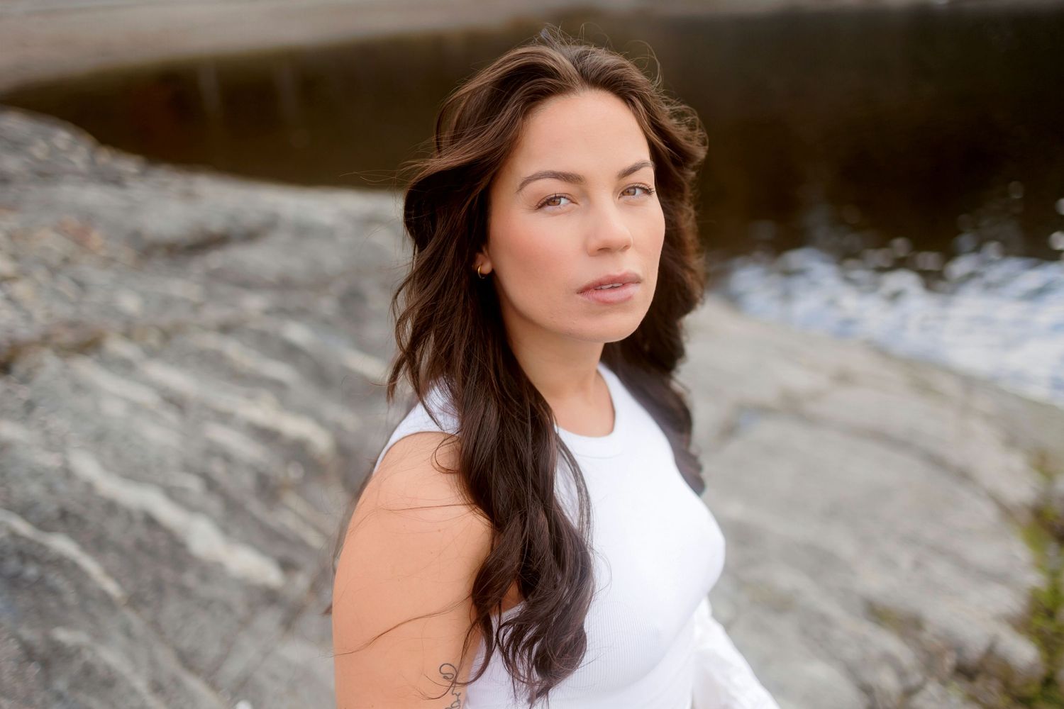 A person in a white dress poses gracefully against a rocky outdoor backdrop during a photo session.