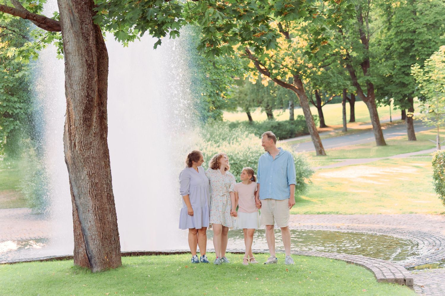 Family in matching blue outfits walking together through a sunlit park on a summer day.
