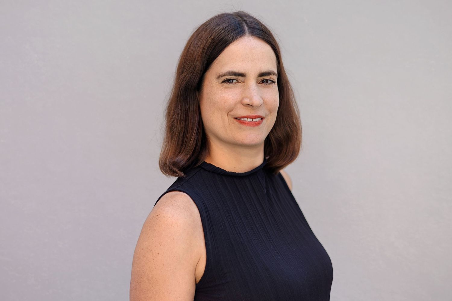 Professional headshot of someone in a sleeveless black top against a light gray background.