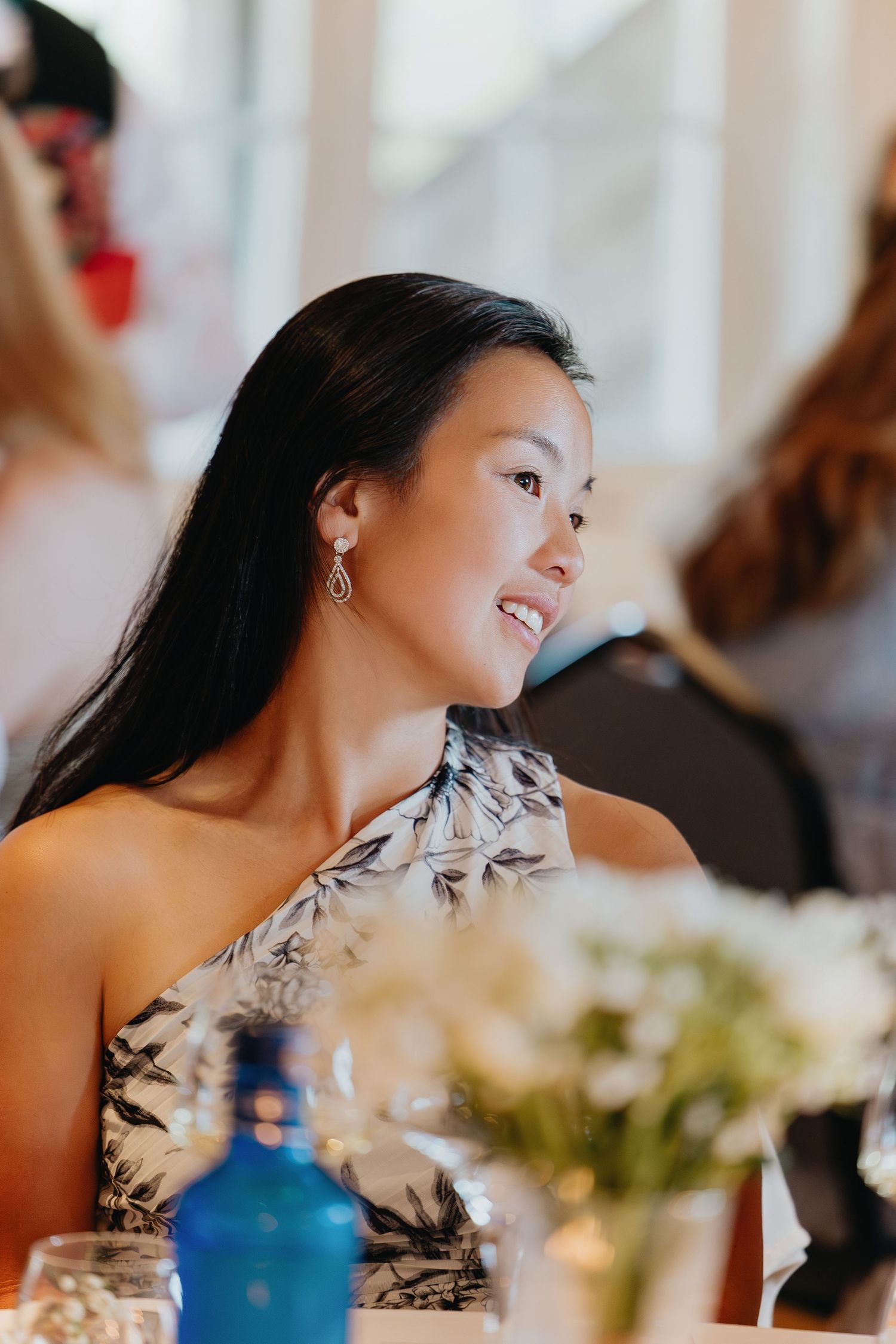 A person in a sleeveless dress laughs joyfully during a reception with floral centerpieces and blurred background.