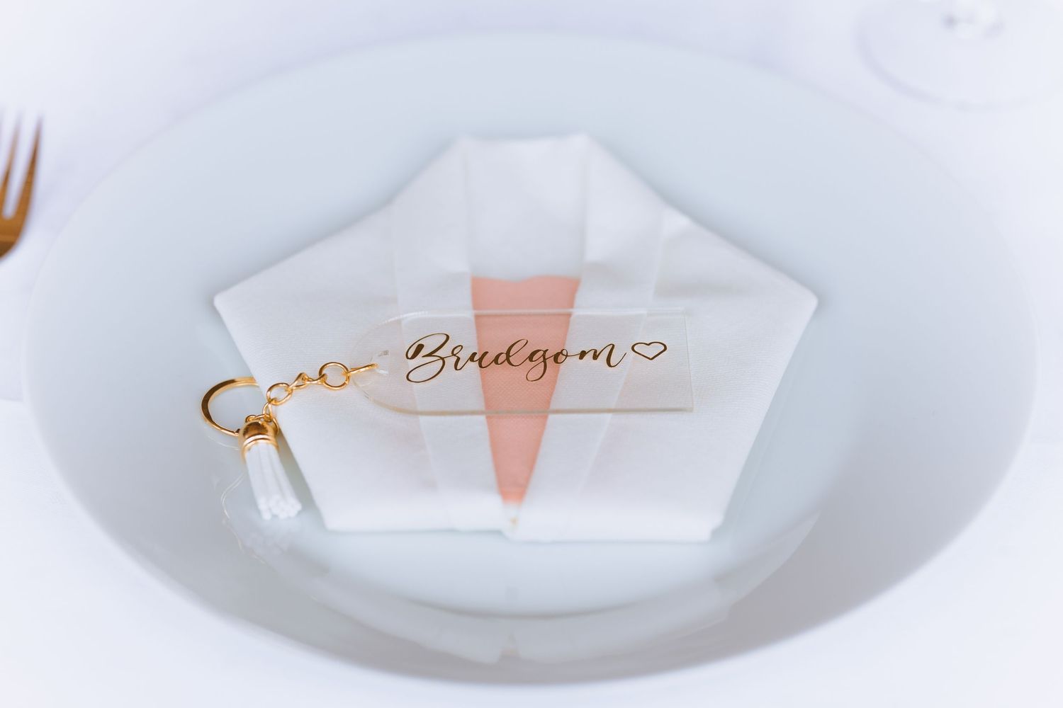 White ceramic plates with elegant pink and gold wedding place cards arranged in a minimalist table setting display.