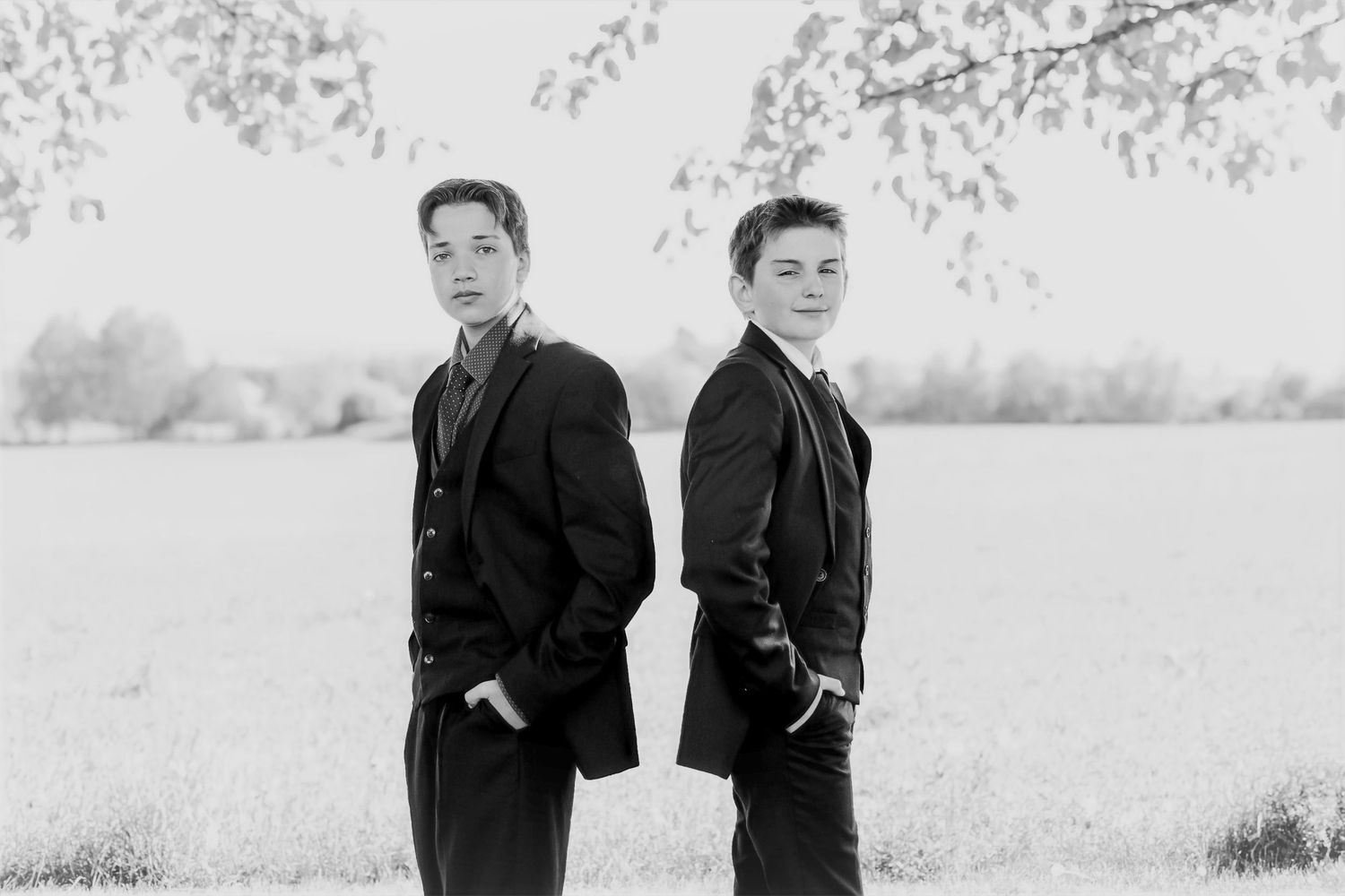 Two people in dark coats stand together in a black and white photograph with a snowy winter landscape behind them.