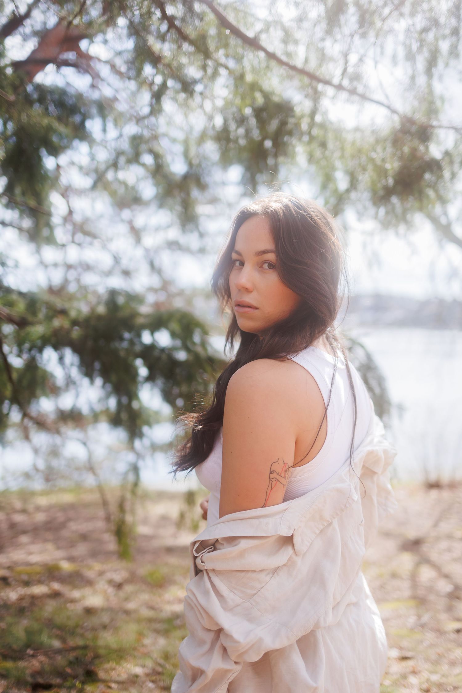 A woman in a flowing white dress poses gracefully in a dreamy outdoor setting with soft natural lighting.