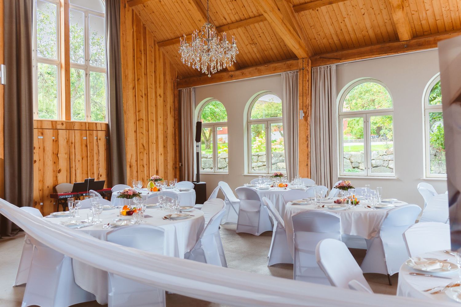 An elegant wedding venue interior with wooden beam ceiling, crystal chandelier and tables set with white linens.