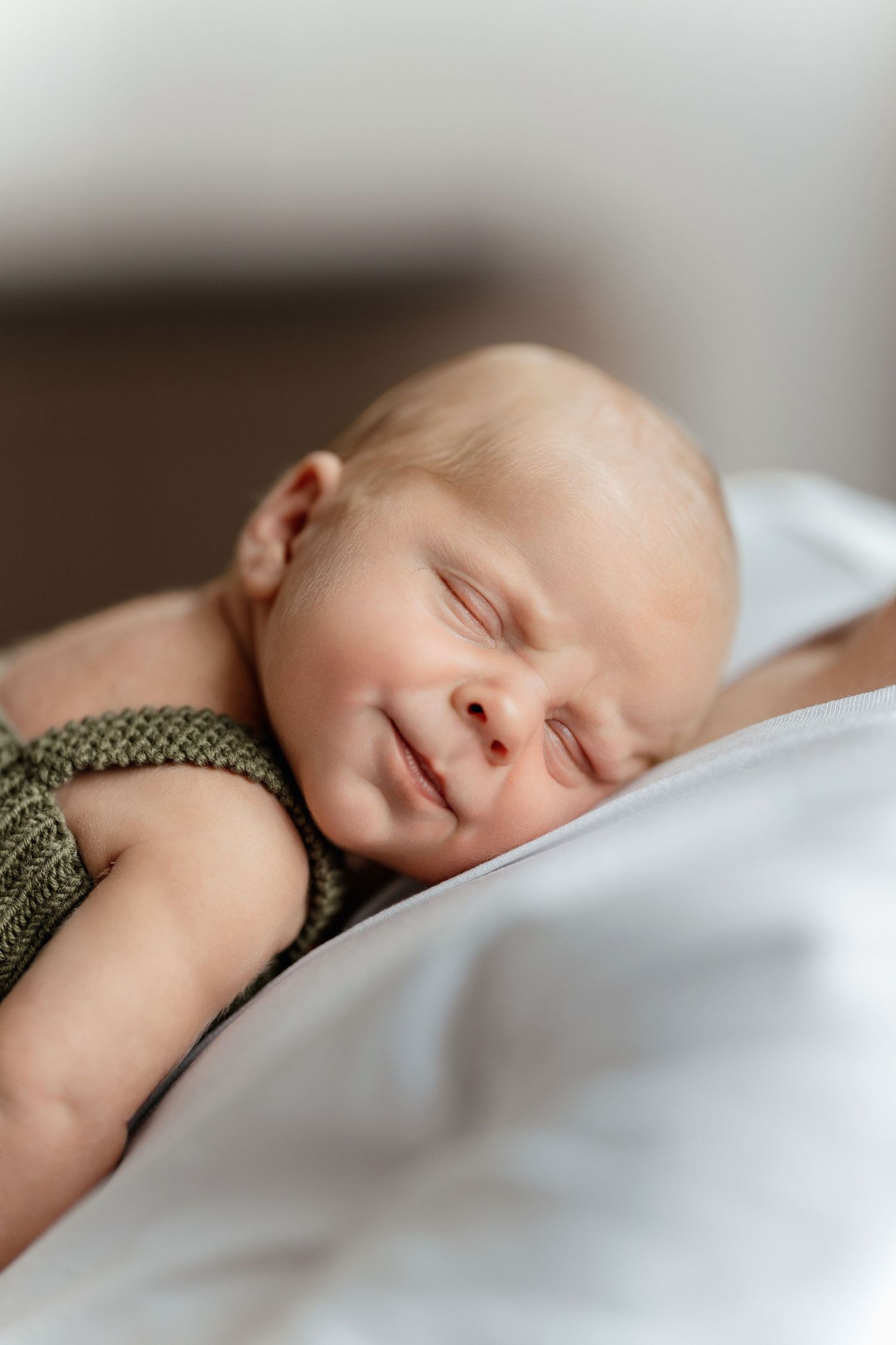 A peaceful newborn baby sleeping in a green knit romper on a soft white blanket.
