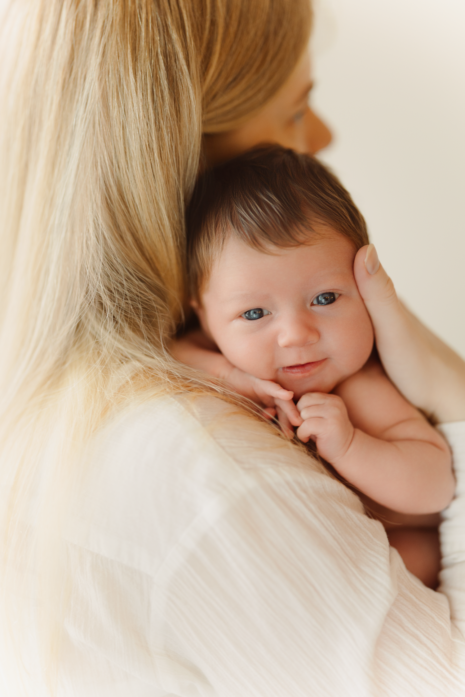 A tender moment between parent and baby with soft lighting and blonde hair visible in a nurturing close-up portrait.