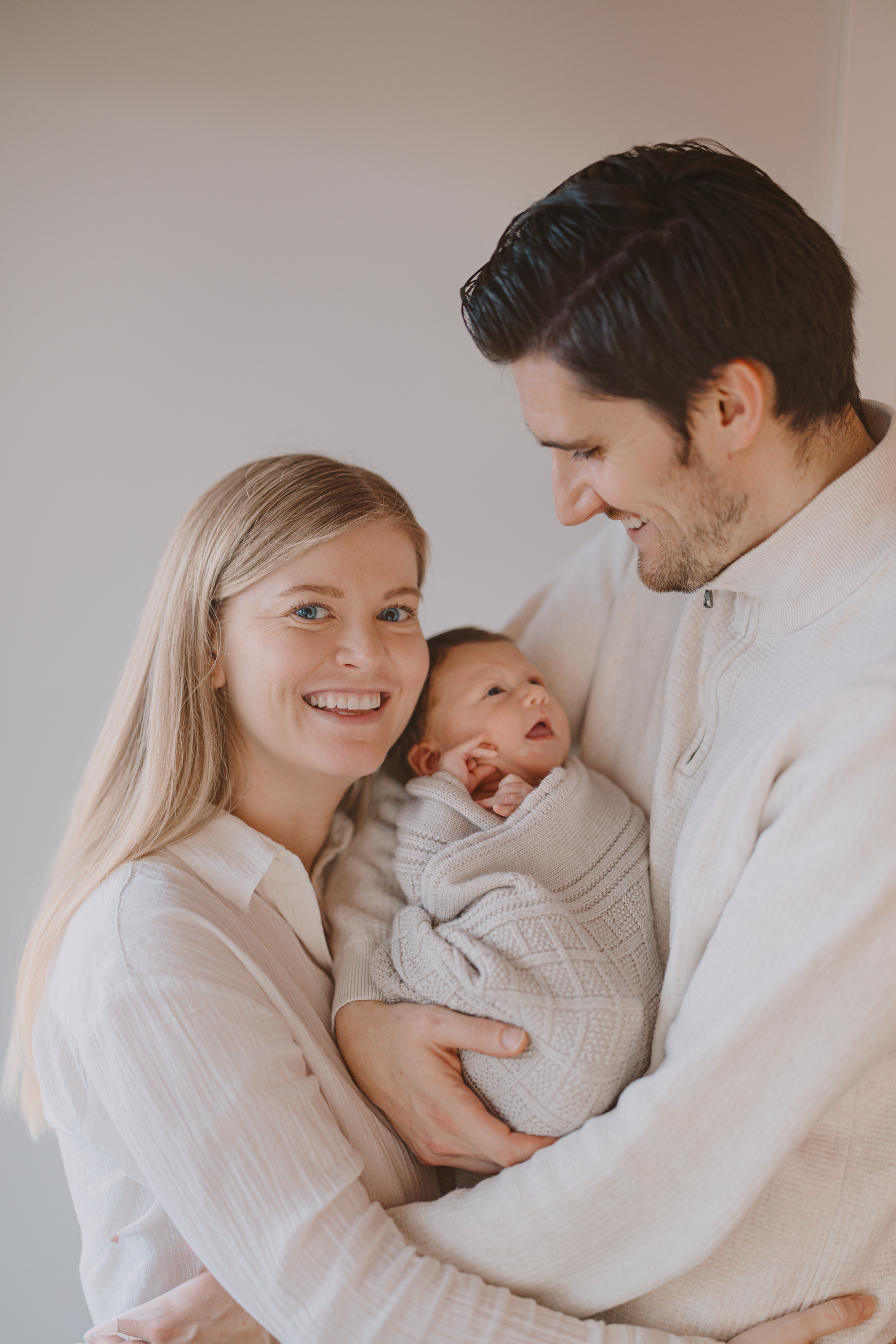Family wearing cozy white sweaters share tender moments together in a bright minimalist setting.