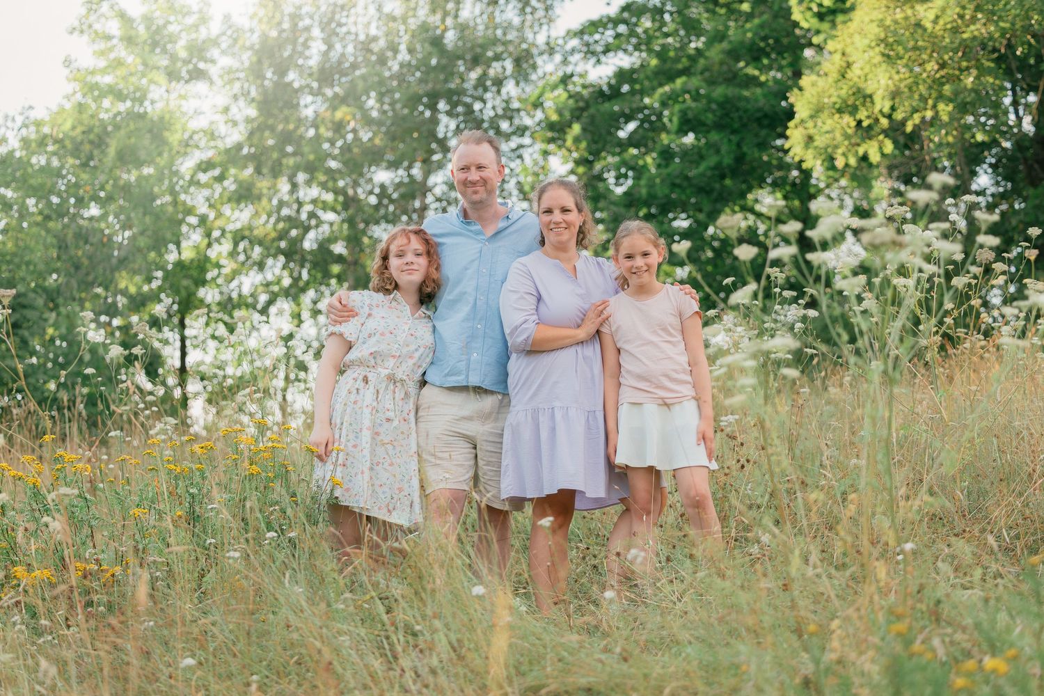 Family portrait in coordinating blue and white outfits among wildflowers and tall grass.