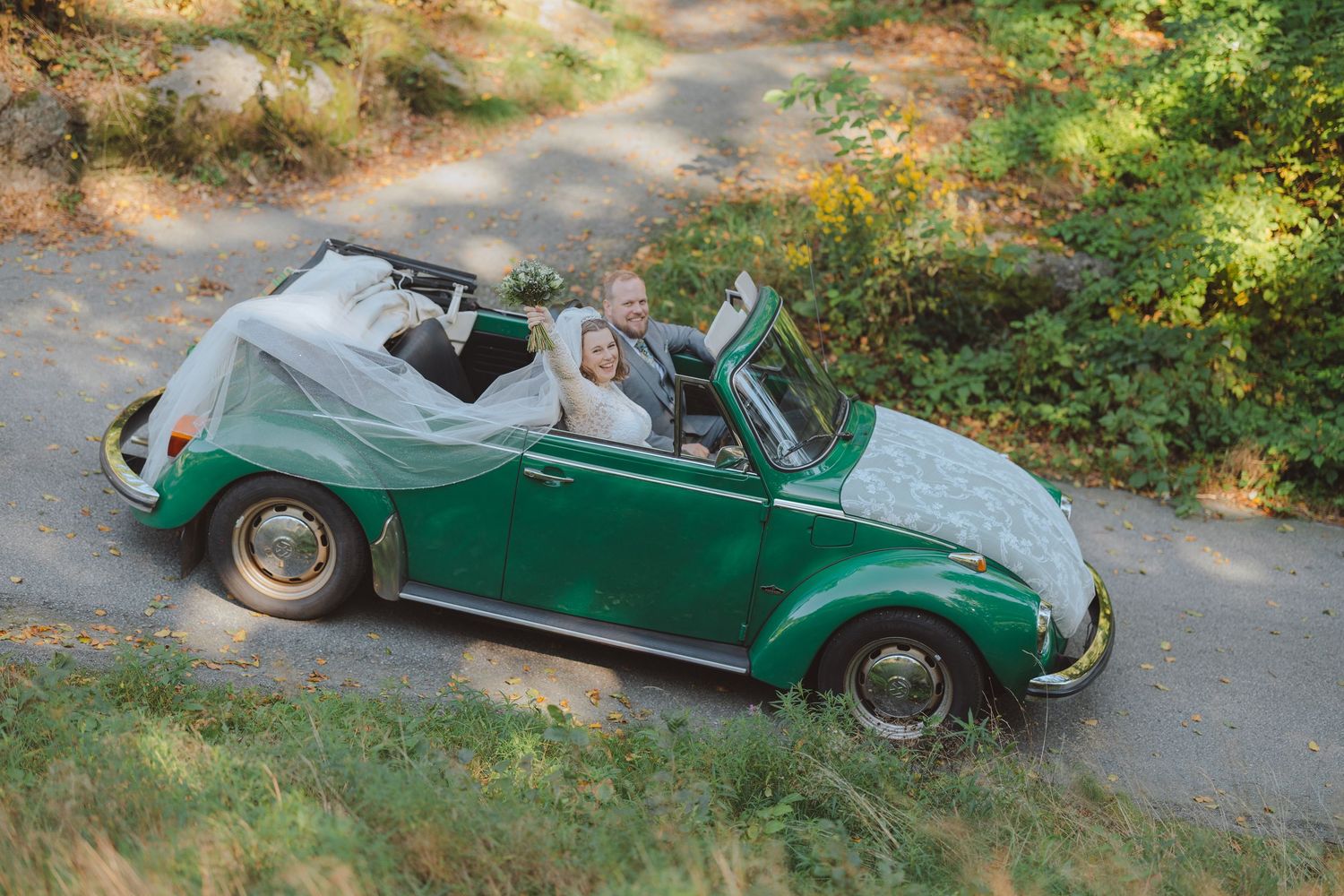 A vintage green convertible car parked on a winding forest path during autumn.