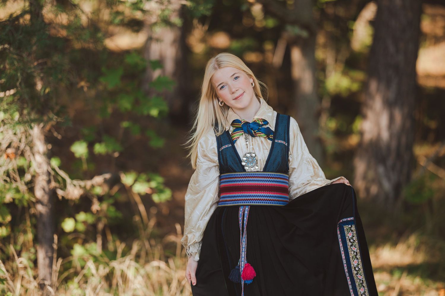 Person in vintage-inspired dress poses in a wooded outdoor setting with natural autumn lighting and foliage.