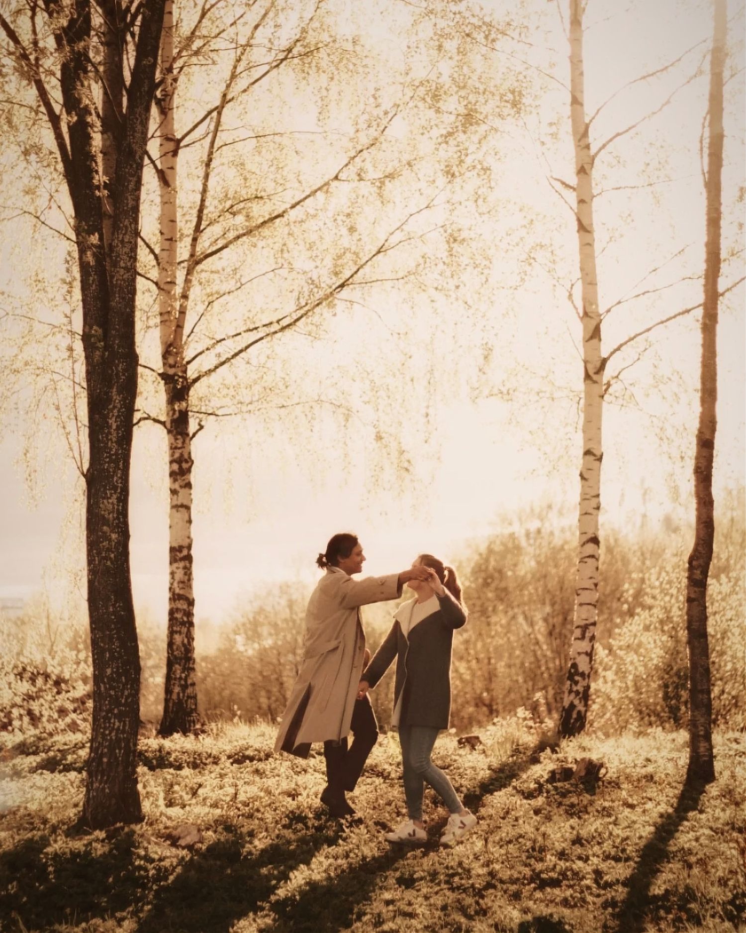 A couple holds hands while walking through a misty forest at sunset creating a romantic silhouette against golden light.