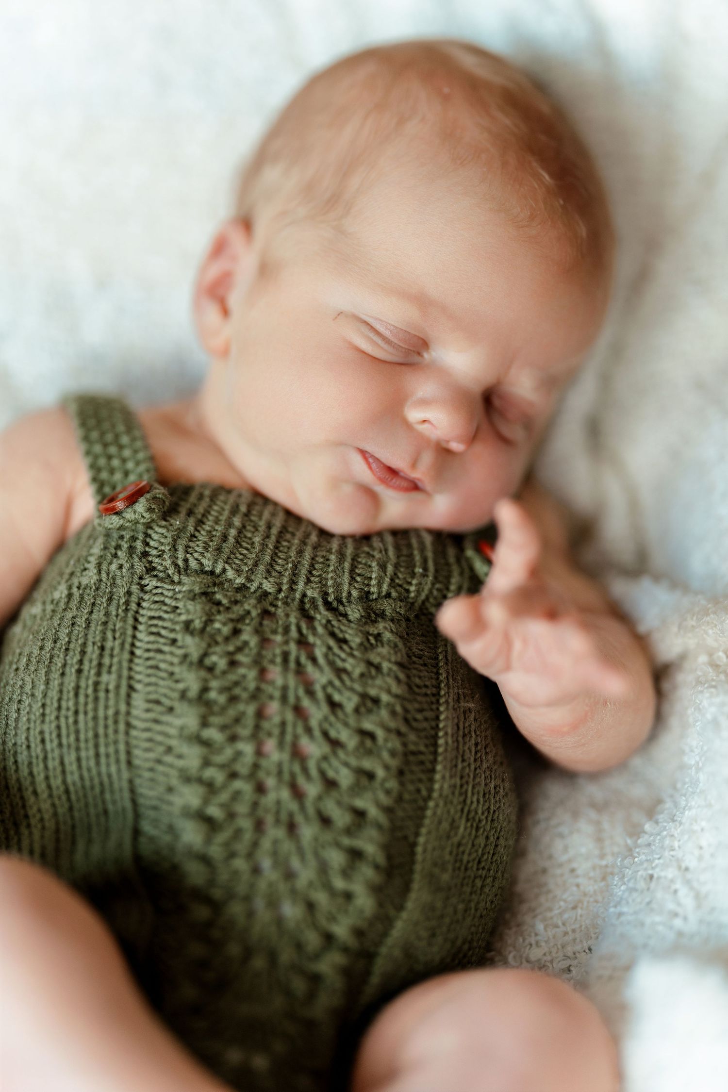 Peaceful newborn baby sleeping in a green knit romper on a soft white blanket.