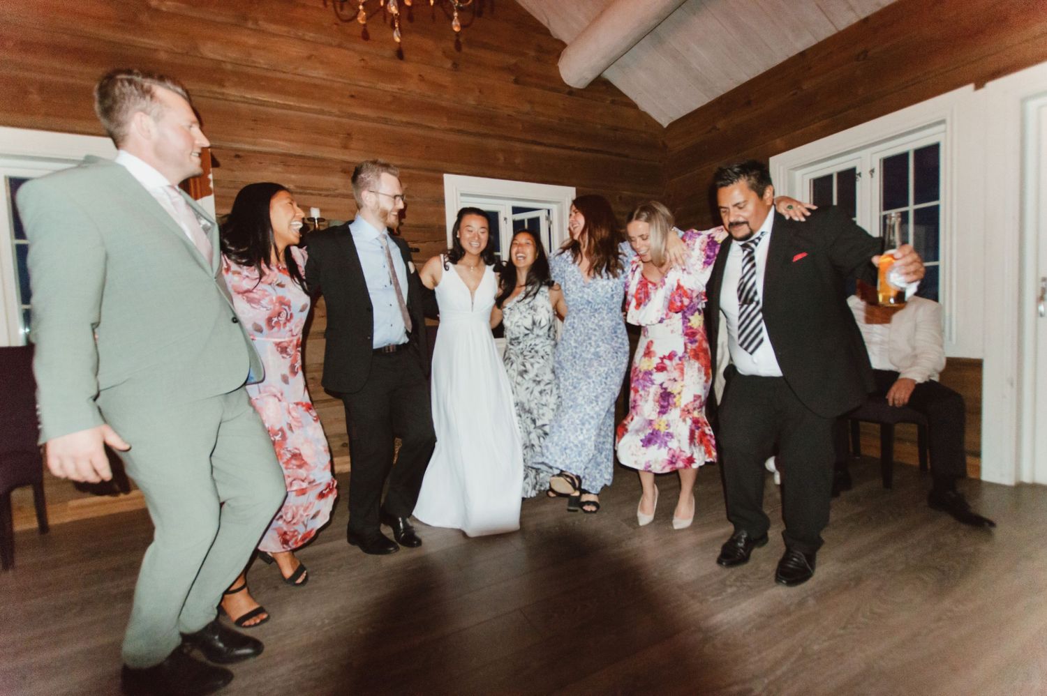 Wedding guests dance and celebrate together on a wooden floor during a reception party.