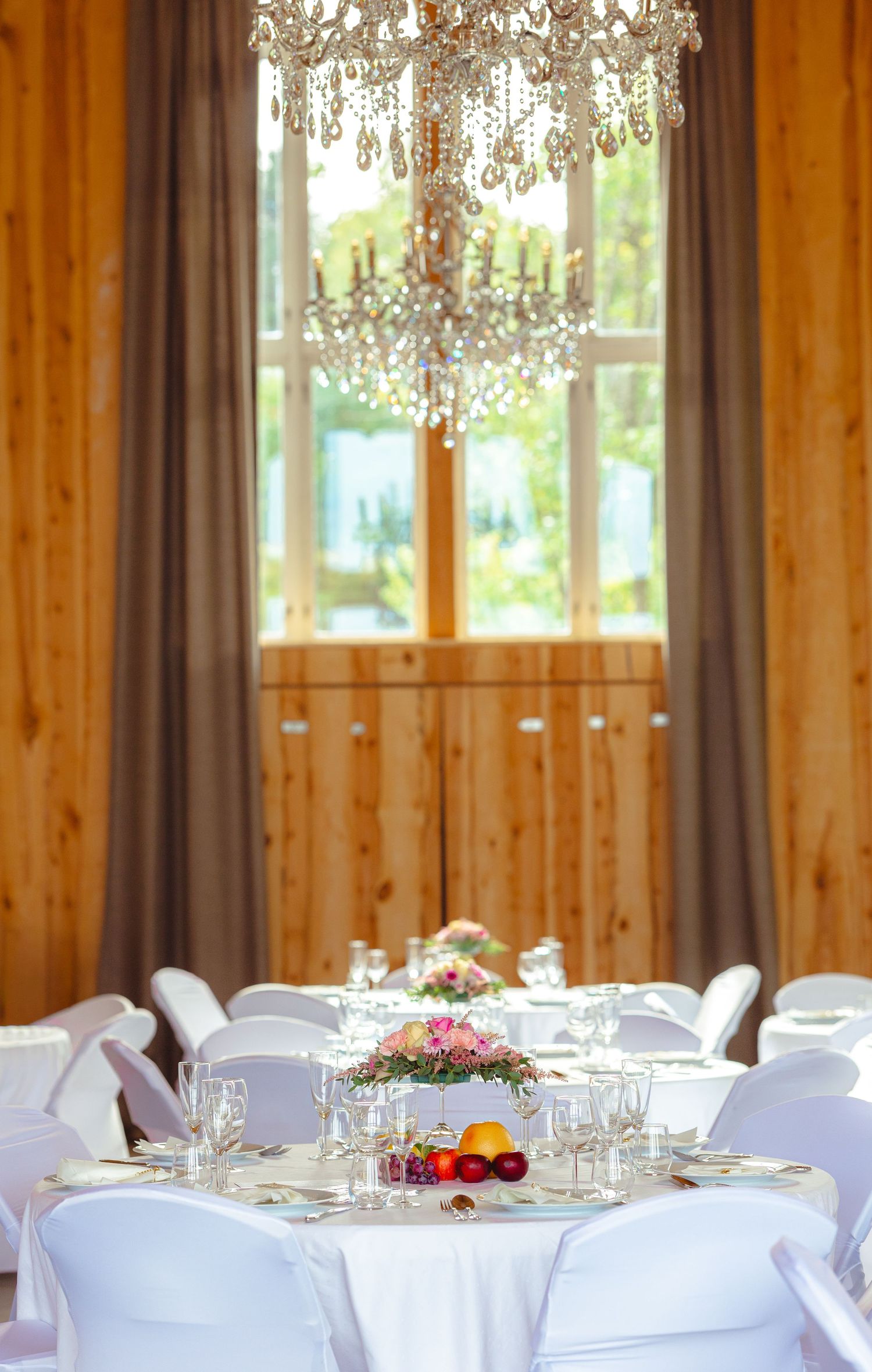 Elegant wedding reception venue with white tablecloths and rustic wooden walls illuminated by natural light.