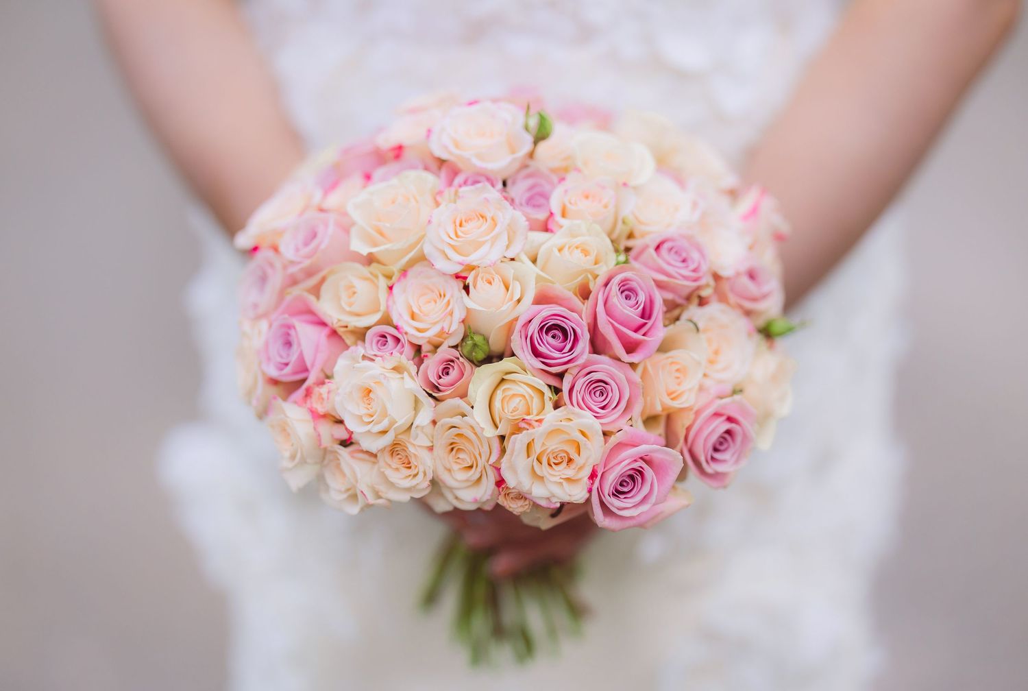 A stunning bridal bouquet of pink and peach roses in a round arrangement against a soft blurred background.