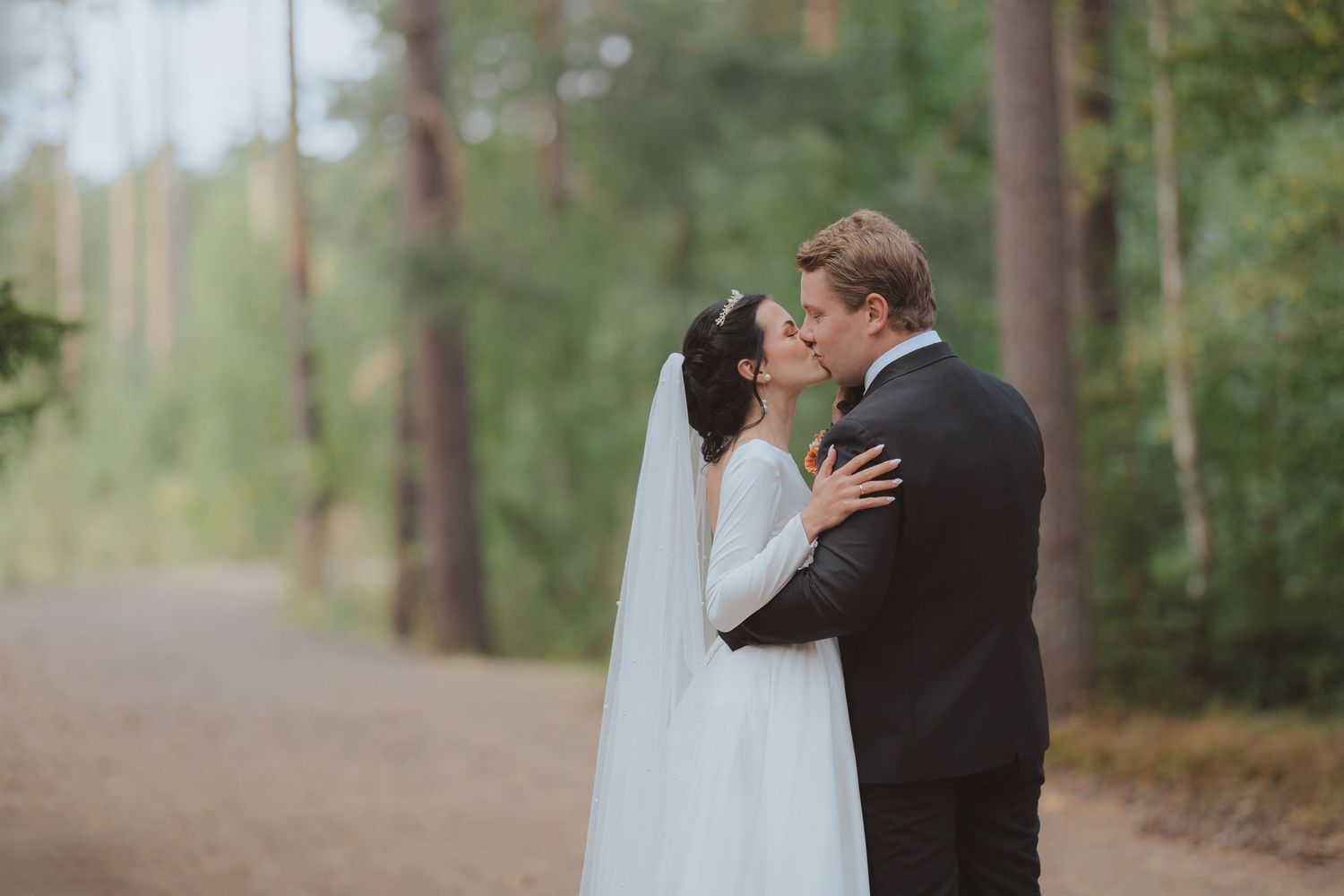 A couple in wedding attire shares intimate moments while walking through a serene forest setting.