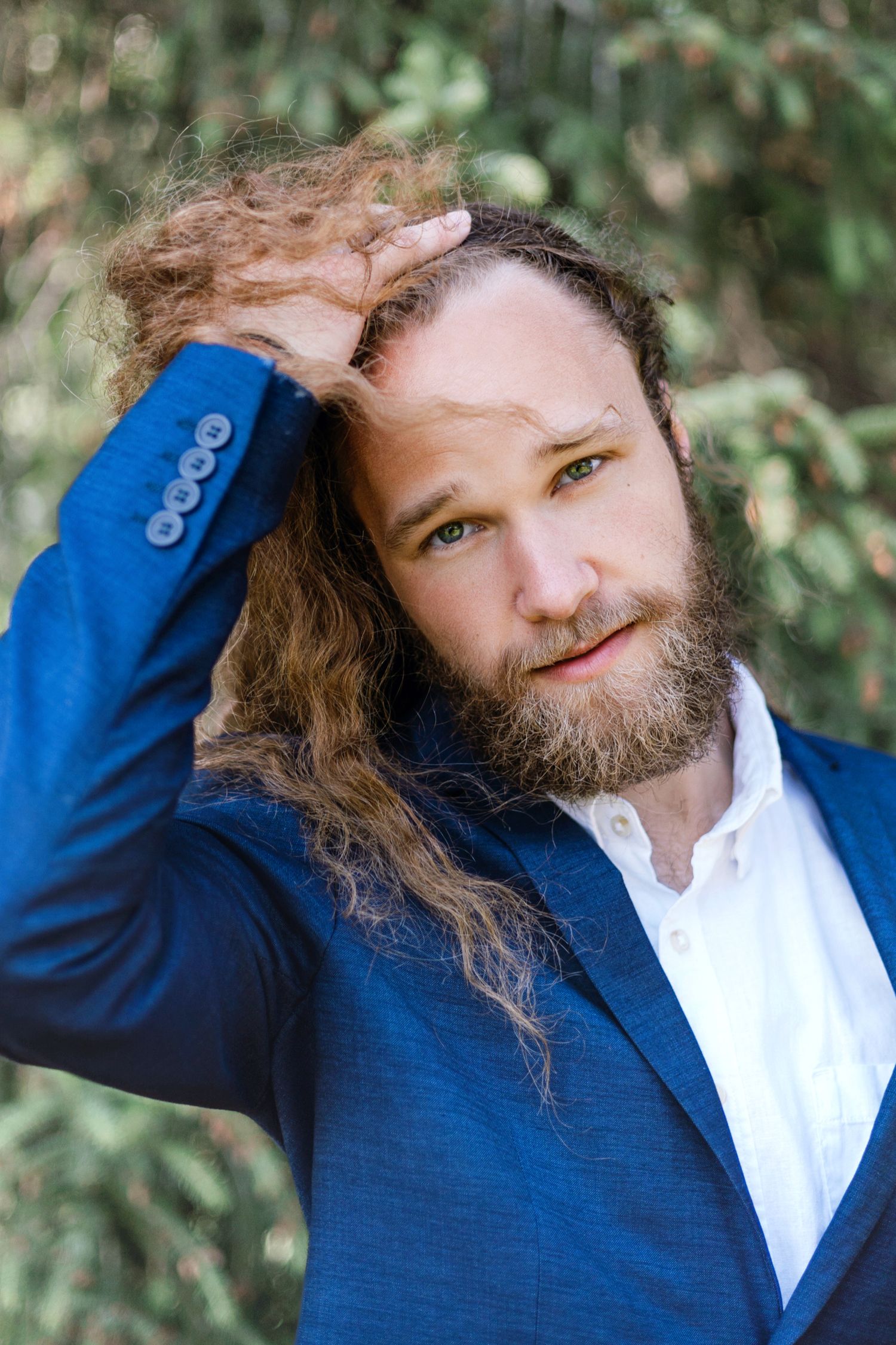 Person wearing a blue blazer and white shirt poses outdoors against a natural green background in a casual style.