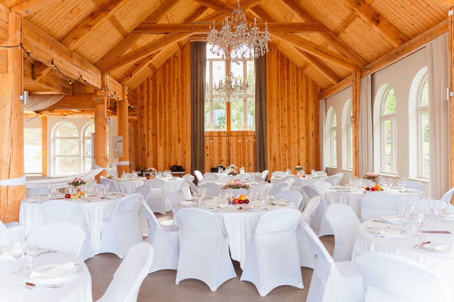 Elegant wedding reception venue with wooden beams, white chairs, and cathedral windows in a rustic chapel setting.