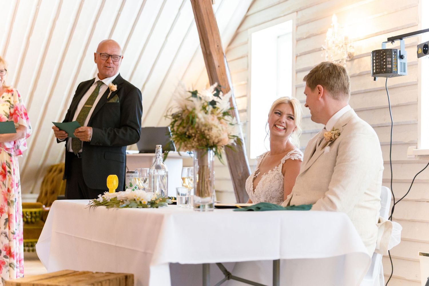 A panoramic view of a wedding reception with guests seated at long white-clothed tables in an elegant venue.
