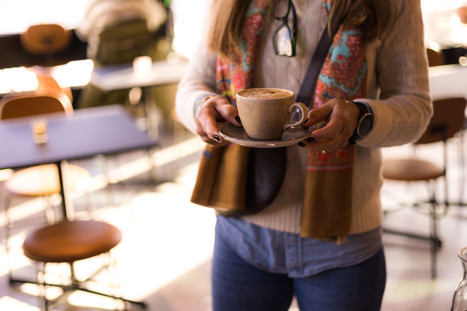 Coffee cups and drinks being served in a warm, sunlit cafe setting.