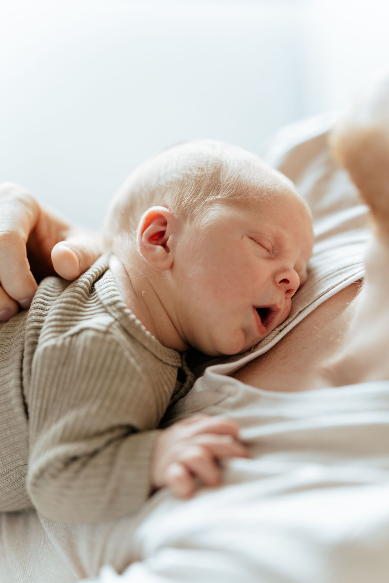 Newborn baby yawning while being held against mother's chest, dressed in a soft ribbed onesie.
