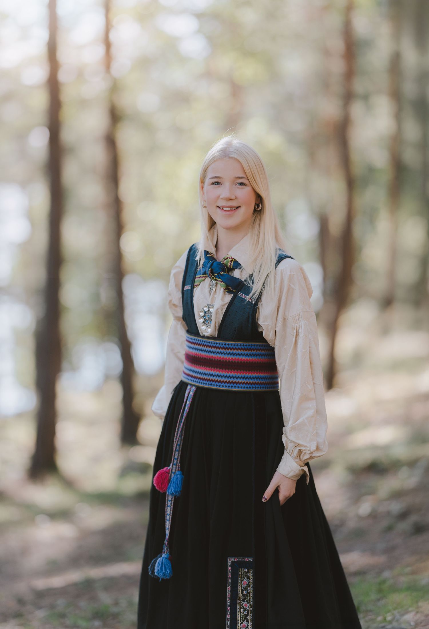 Traditional folk dress with embroidered details and tassels photographed in a forest setting.