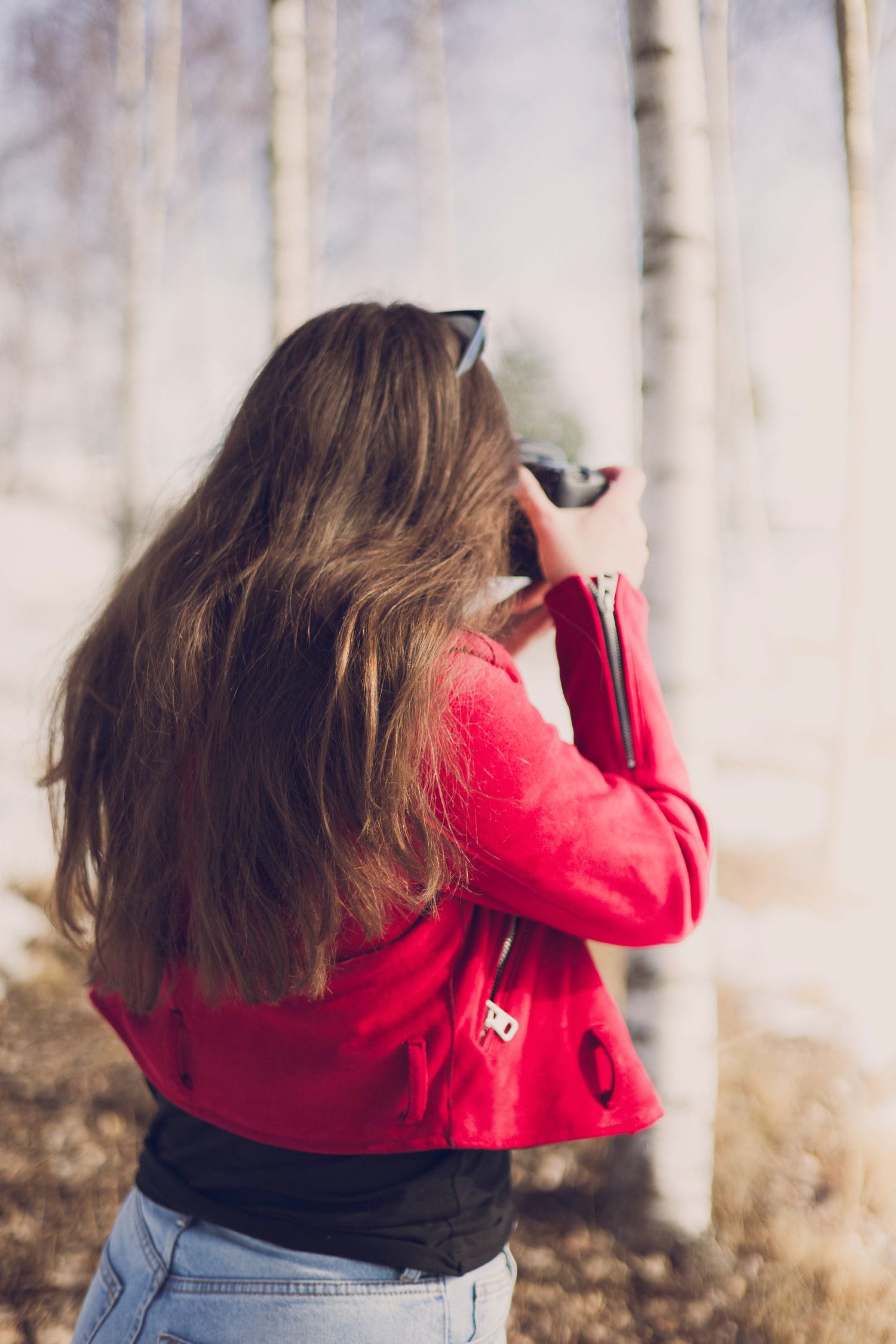 Photographer in red jacket taking pictures among birch trees in winter landscape.