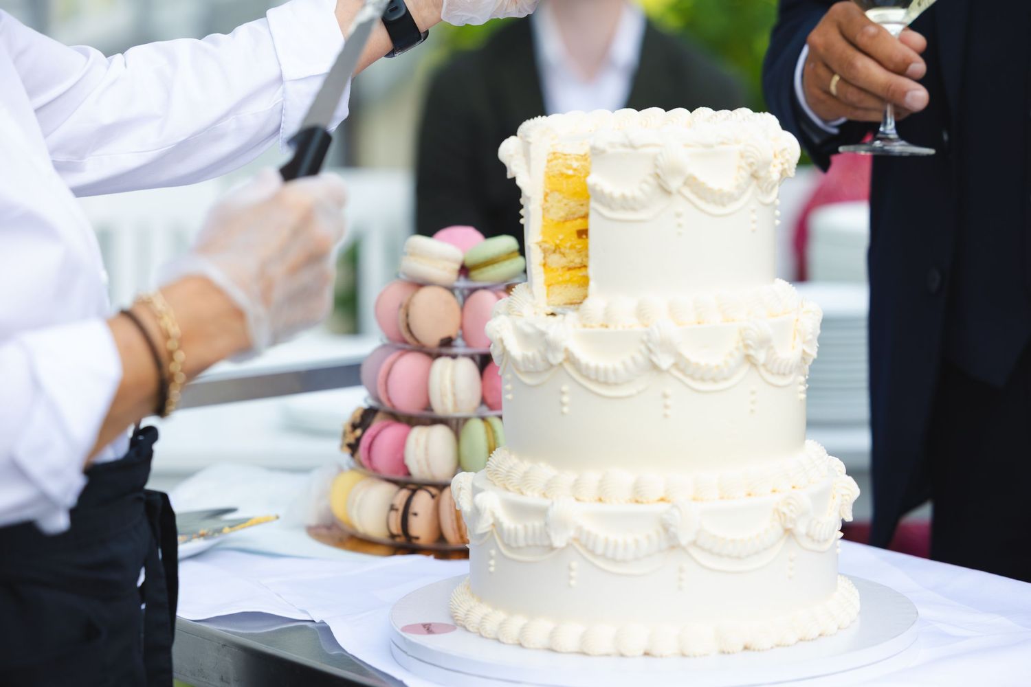 A row of white wedding cakes being cut and served at an elegant reception.
