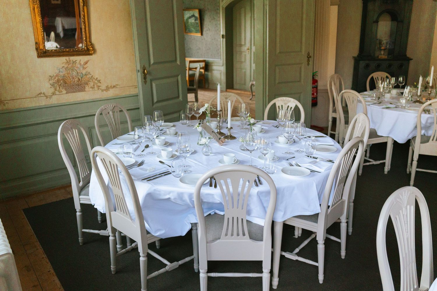 Elegant dining room setup with round tables covered in white linens and white chairs in a classic interior space.
