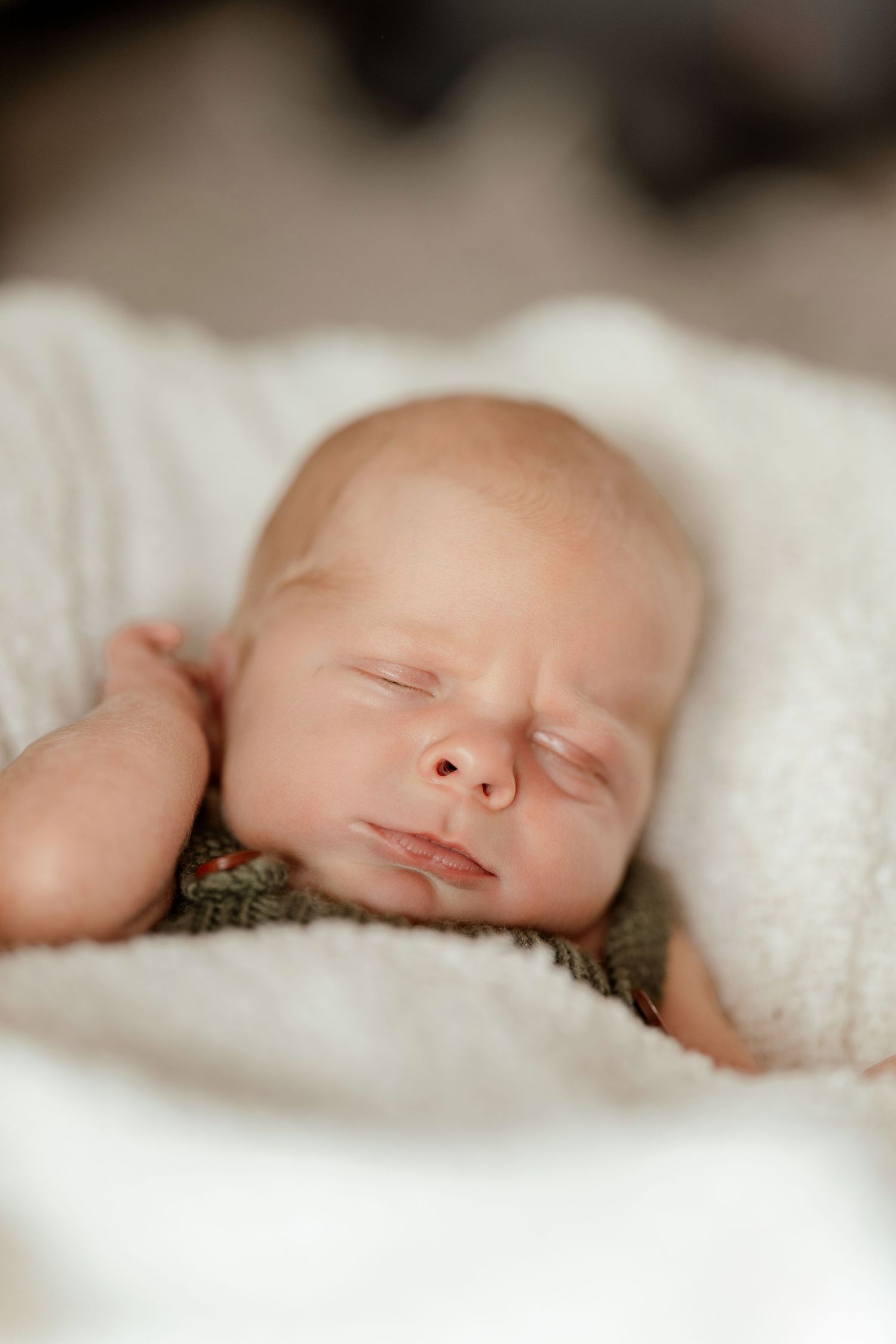 Peaceful newborn baby sleeping soundly wrapped in a soft white blanket, wearing a green knit outfit.