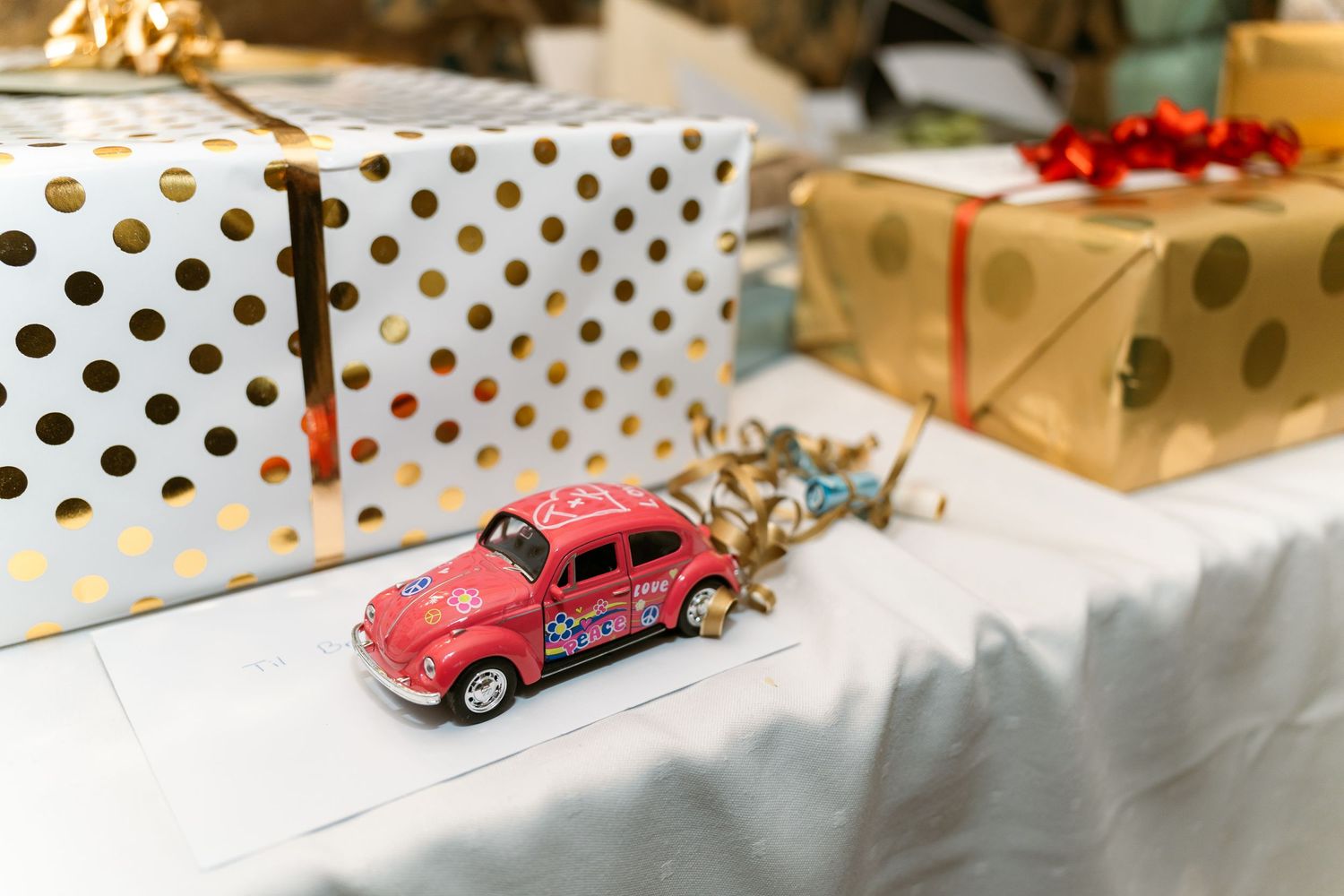 Vintage red Volkswagen Beetle toy car on a polka dot patterned surface with wrapped gifts in the background.