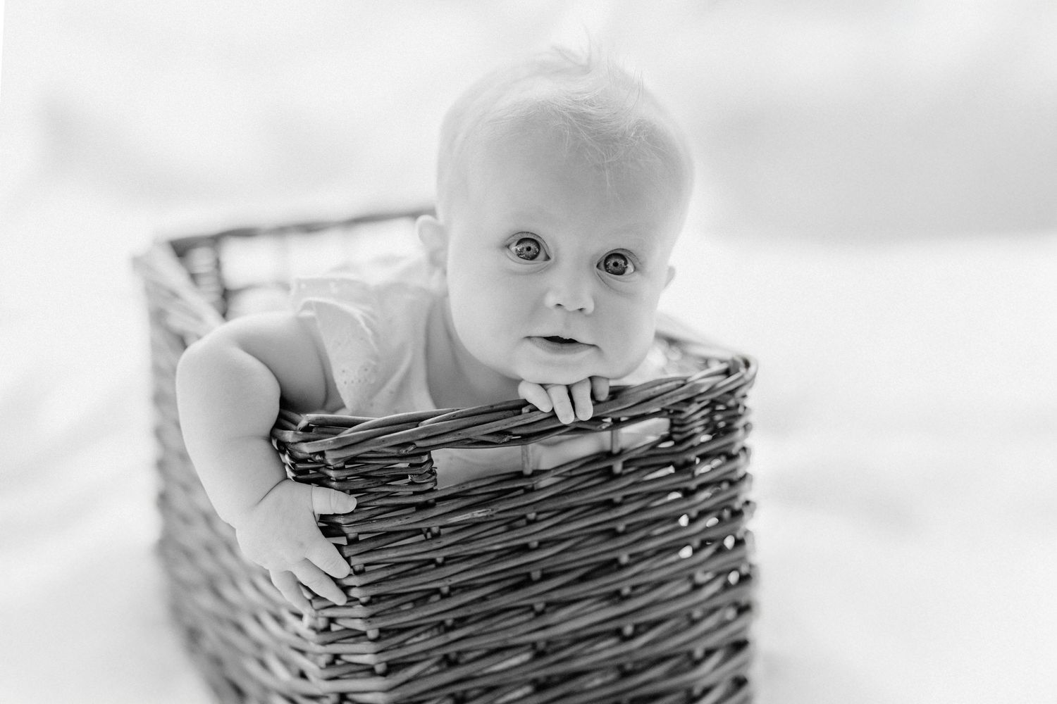 A baby sits inside a rustic wooden basket in a series of black and white photos showing different angles and expressions.