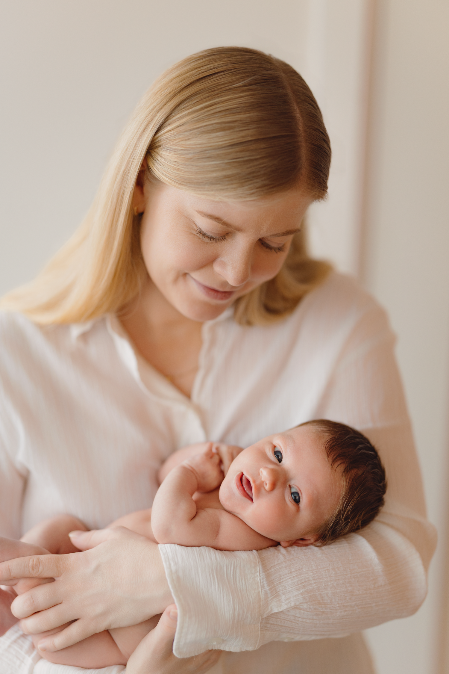 A tender moment between parent and newborn baby in soft natural light against white bedding.