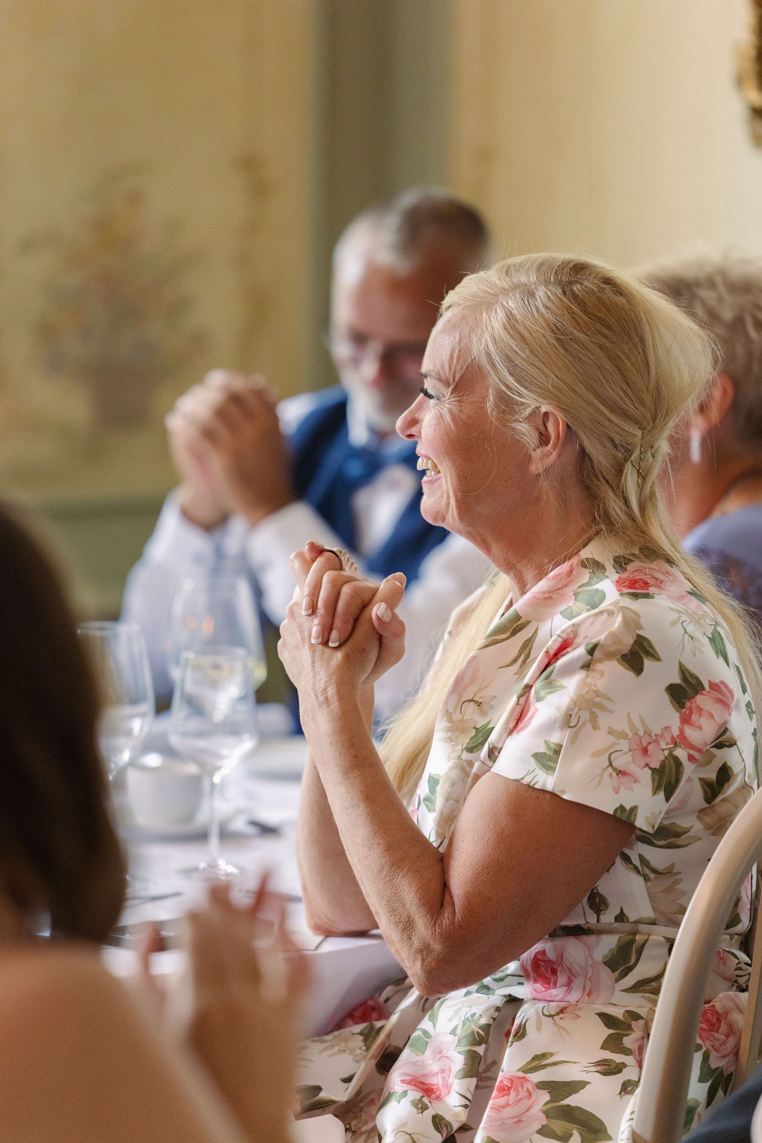 A person wearing a floral print dress sits at a formal dining table during an event.