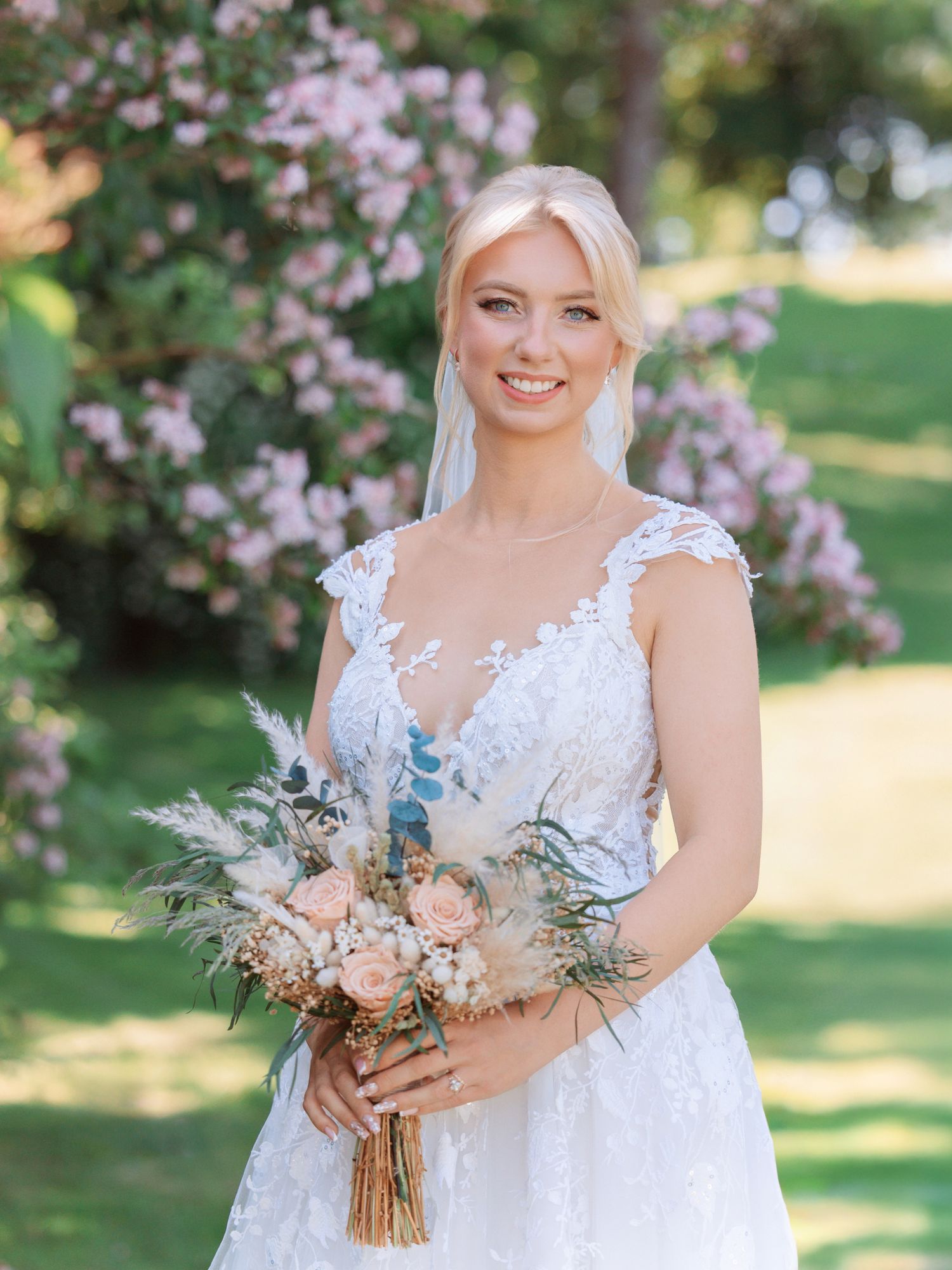 Bridal portrait with delicate lace dress and soft pastel bouquet in a garden setting.