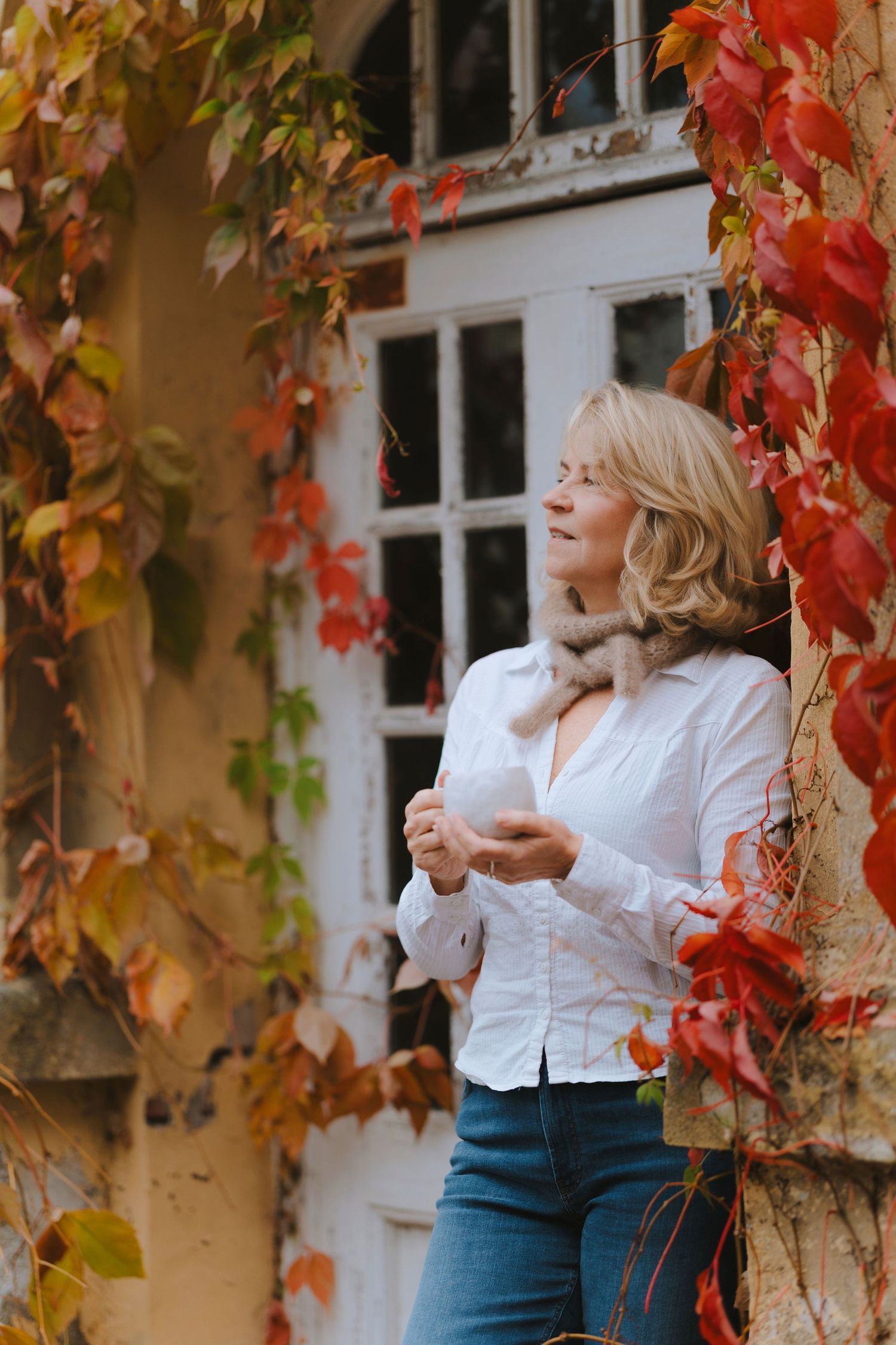 Autumn scene with vibrant red ivy leaves framing white windows and someone in a white shirt and jeans.