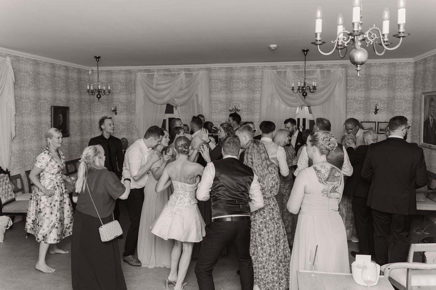 Vintage black and white photograph of couples dancing at a formal event with chandeliers and elegant decor.