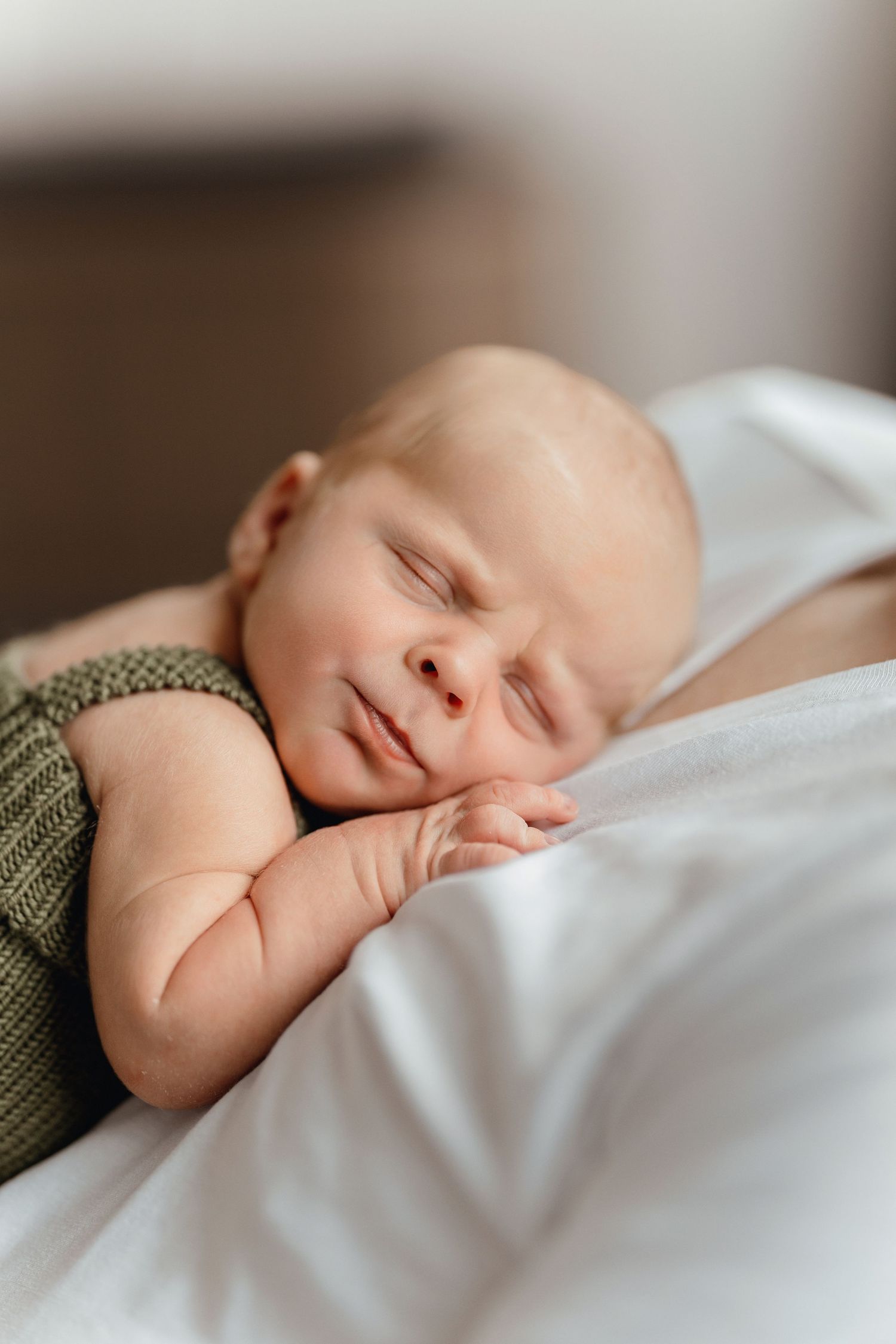 A peaceful newborn baby sleeping soundly, wearing a green knit outfit, resting on a soft white blanket.
